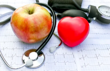 An apple, a red heart-shaped object, and a stethoscope on an electrocardiogram monitor