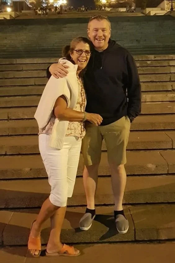 A woman and a man standing on stairs outdoors at night, smiling and hugging each other.