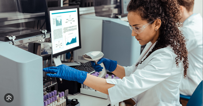 A scientist in protective eyewear and gloves working with lab equipment in a laboratory setting, using a barcode scanner.