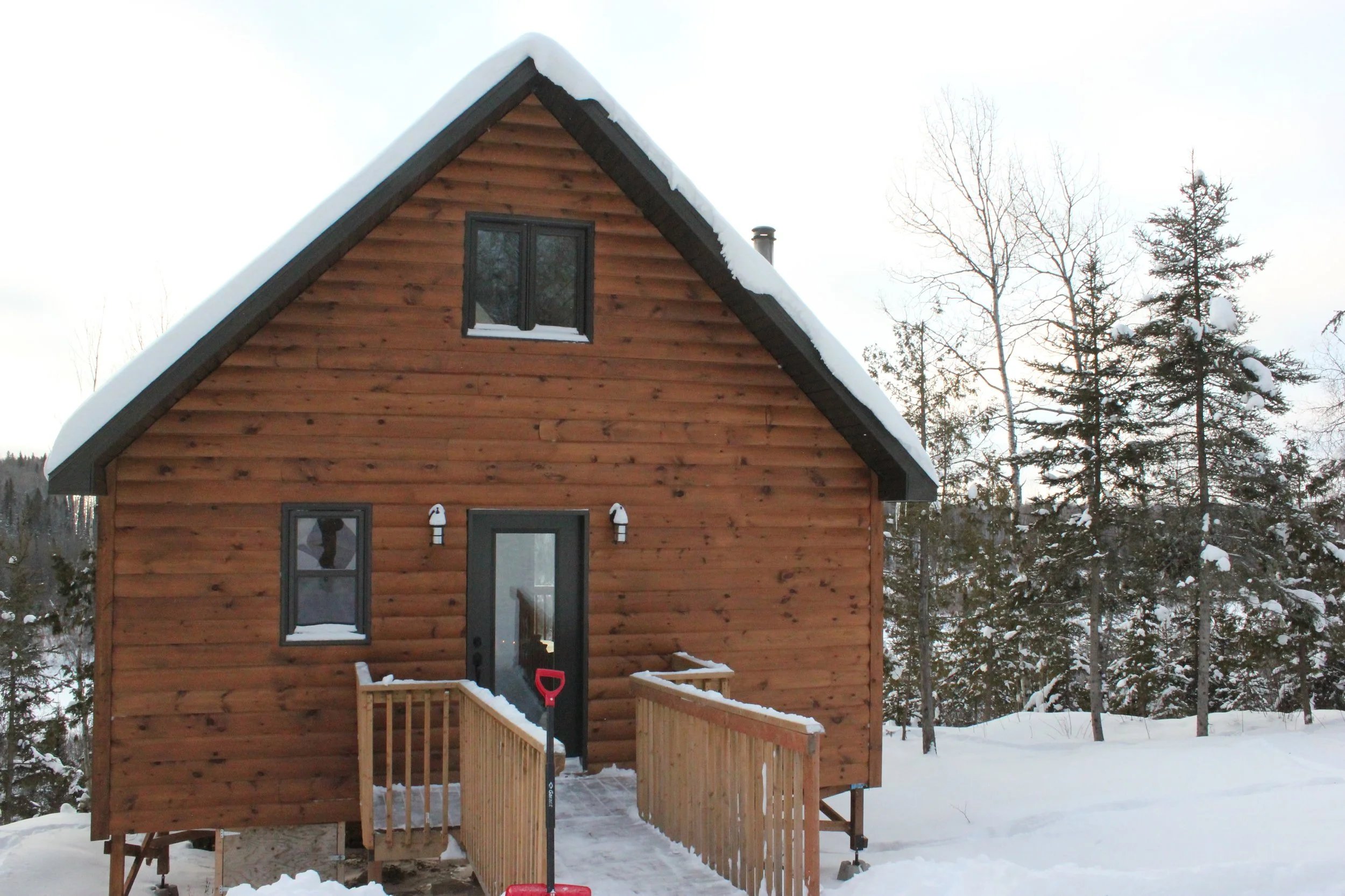 Une maison en bois avec un toit enneigé, entourée d'arbres enneigés, en hiver.