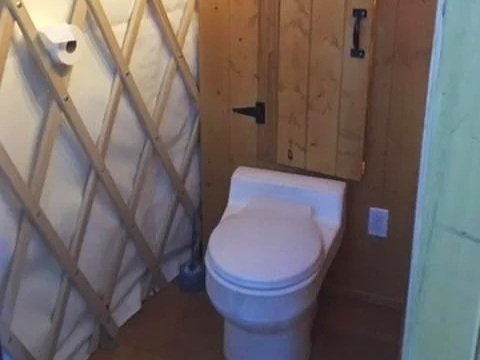 Toilettes dans une salle de bain en bois avec une cloison en planches et un support pour papier toilette