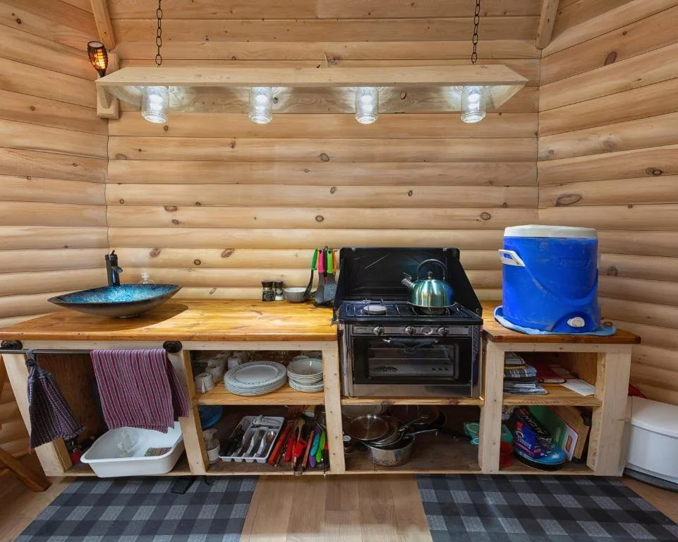 Cuisine rustique en bois avec un évier en pierre, un poêle à gaz, un réfrigérateur-portable bleu, des ustensiles de cuisine, des assiettes et un tapis aux motifs à carreaux.