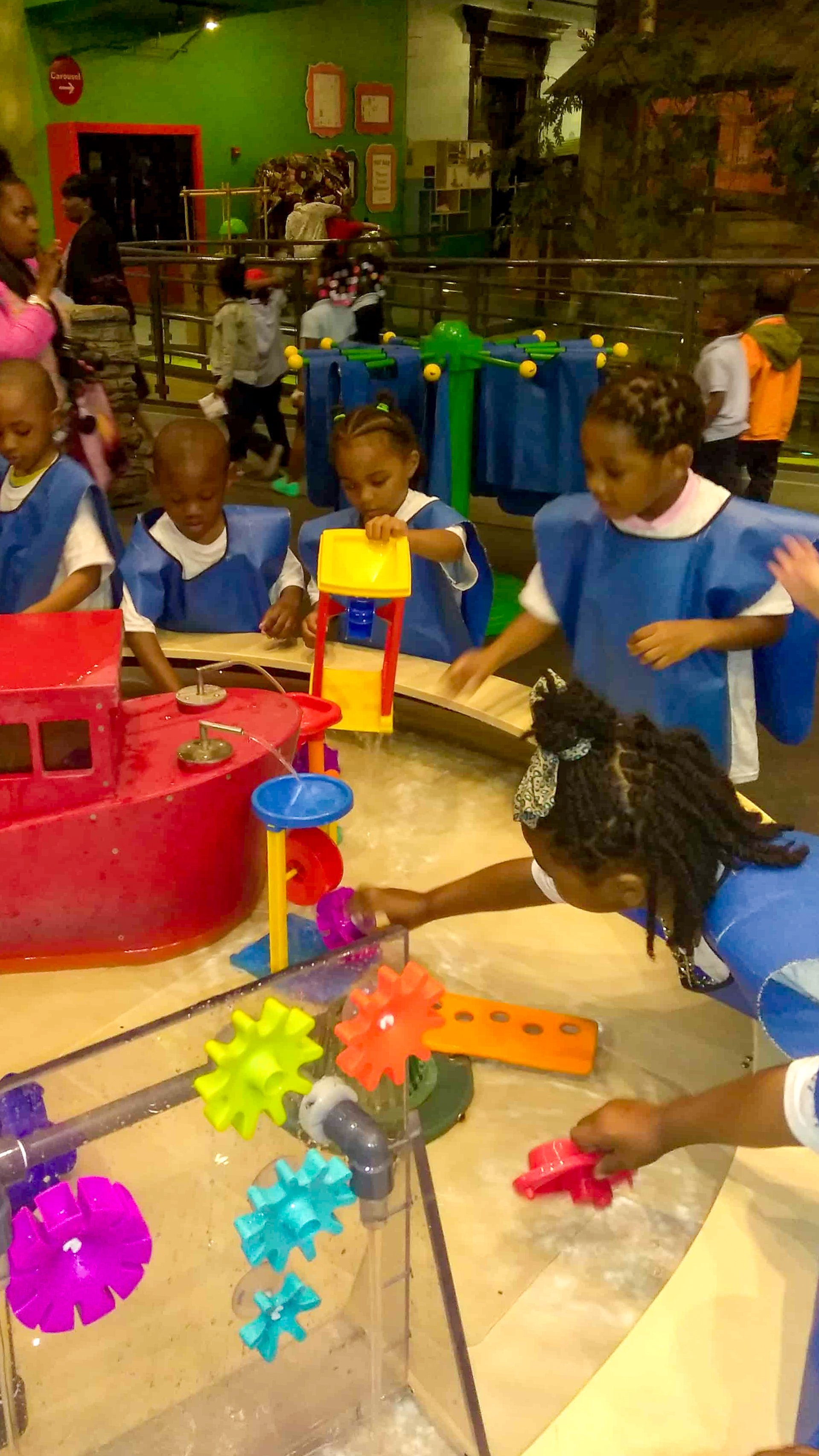 Children playing with a water table and colorful gear toys in a Tots Yearn to Learn indoor play area.