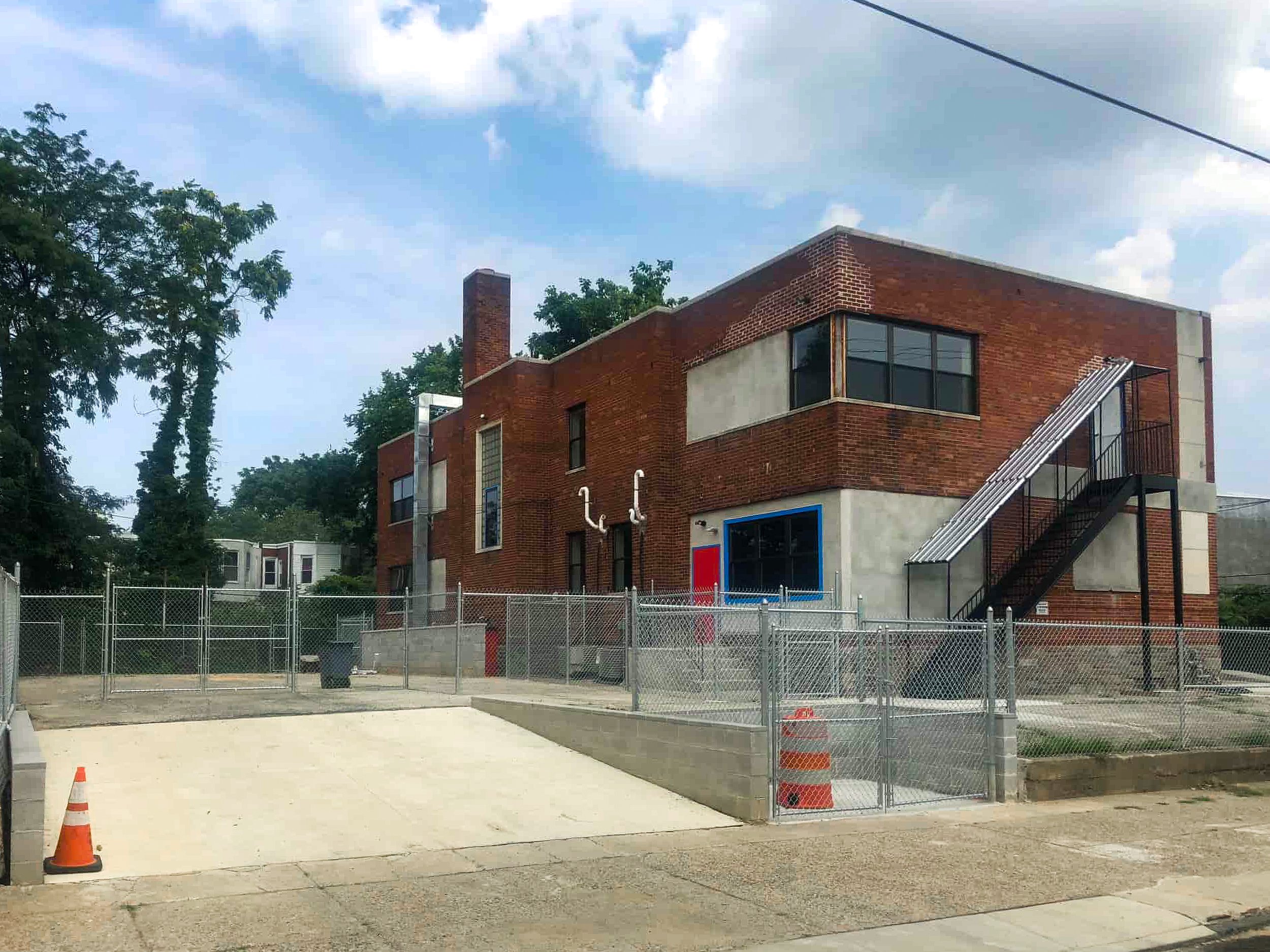 Tots Yearn to Learn Larchwood, a two-story building with a red brick exterior, metal stairs on the right side, and a concrete section on the lower part, surrounded by a fence.