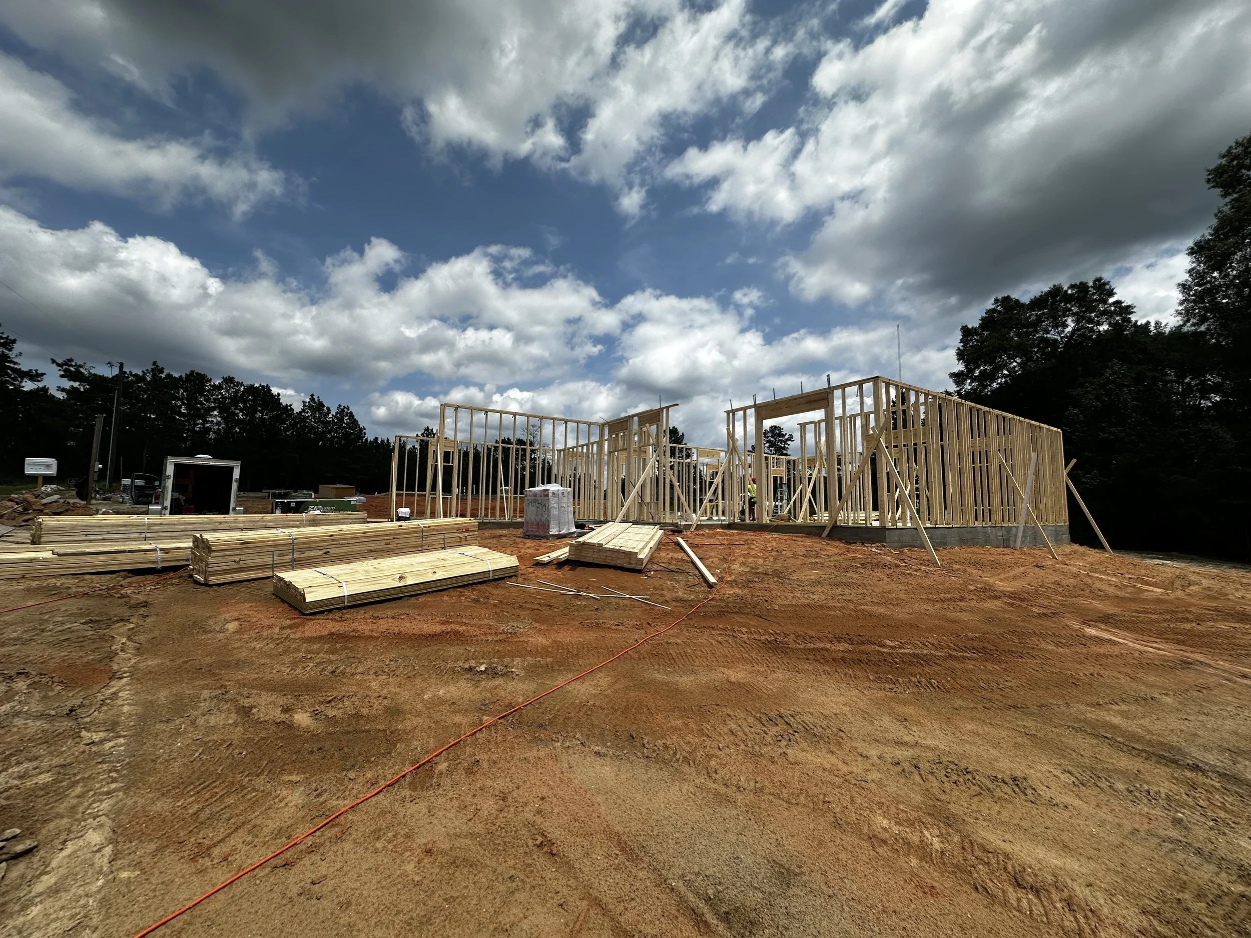Construction site with wooden framing of a building under a partly cloudy sky.