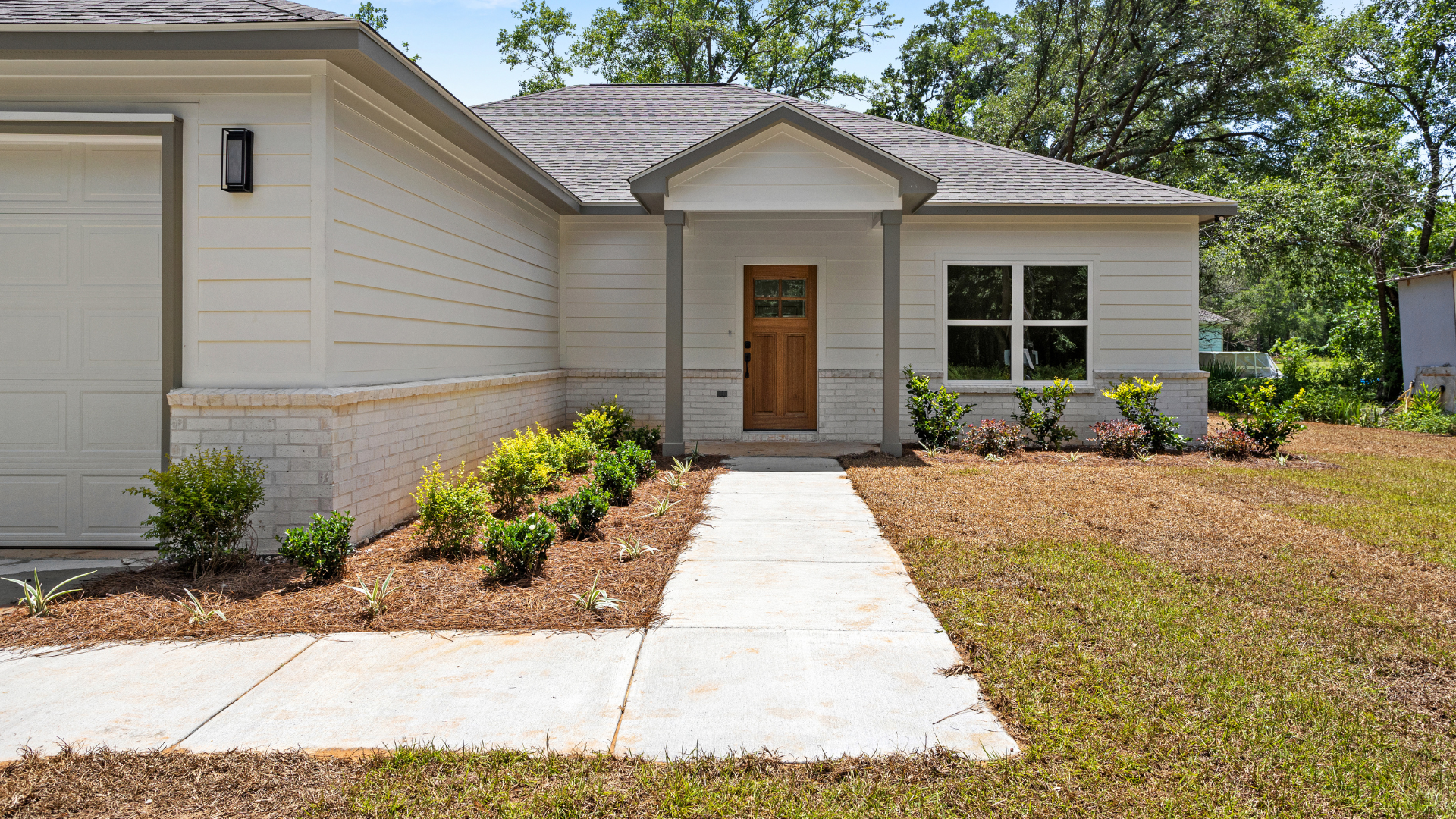 Front of a modern house with a concrete walkway, small bushes, and a wooden front door.