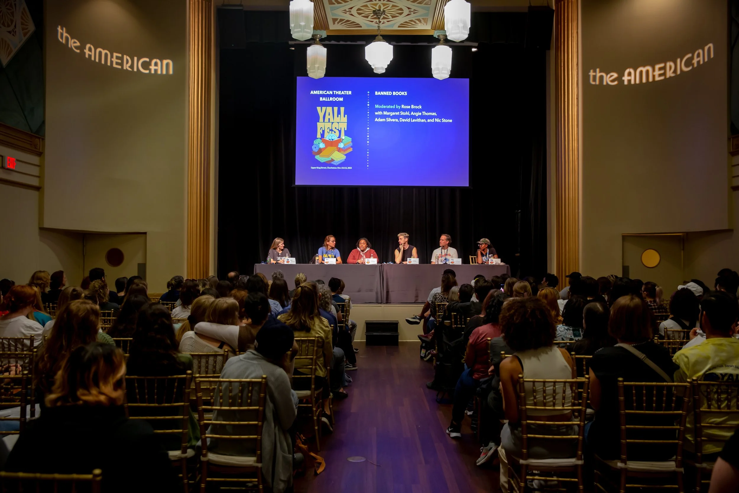 A panel (photo taken from the back, most audience members can be seen from the back and six authors are onstage)