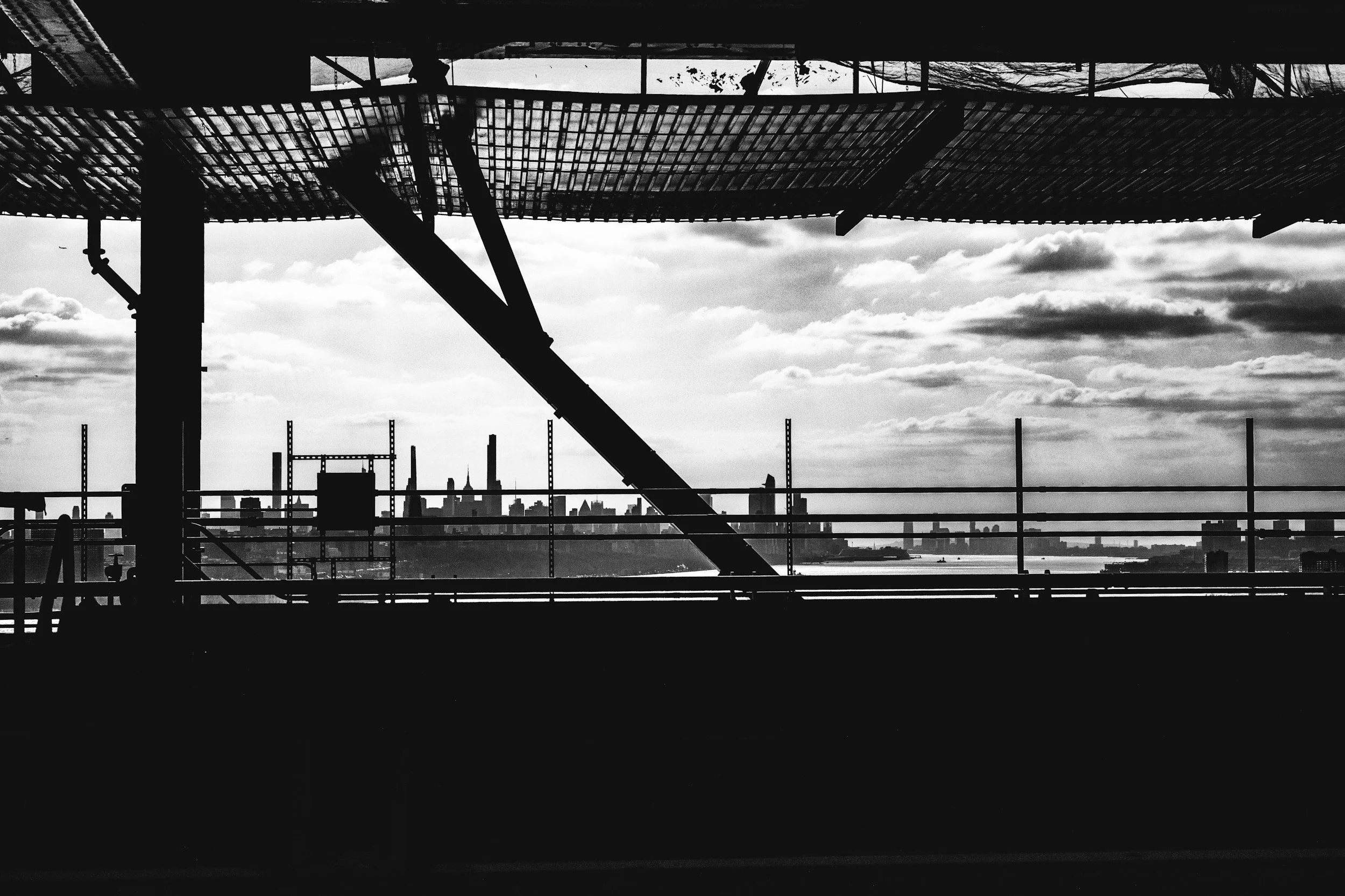Black and white photo of a city skyline viewed from a construction site with metal beams and scaffolding in the foreground.
