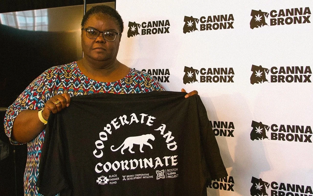 A woman with glasses holding a black flag with white text that reads 'Operate and Coordinate' and a logo of a panther. The background has a repeating pattern of the words 'Canna Bronx' and a map of New York State with a marijuana leaf.