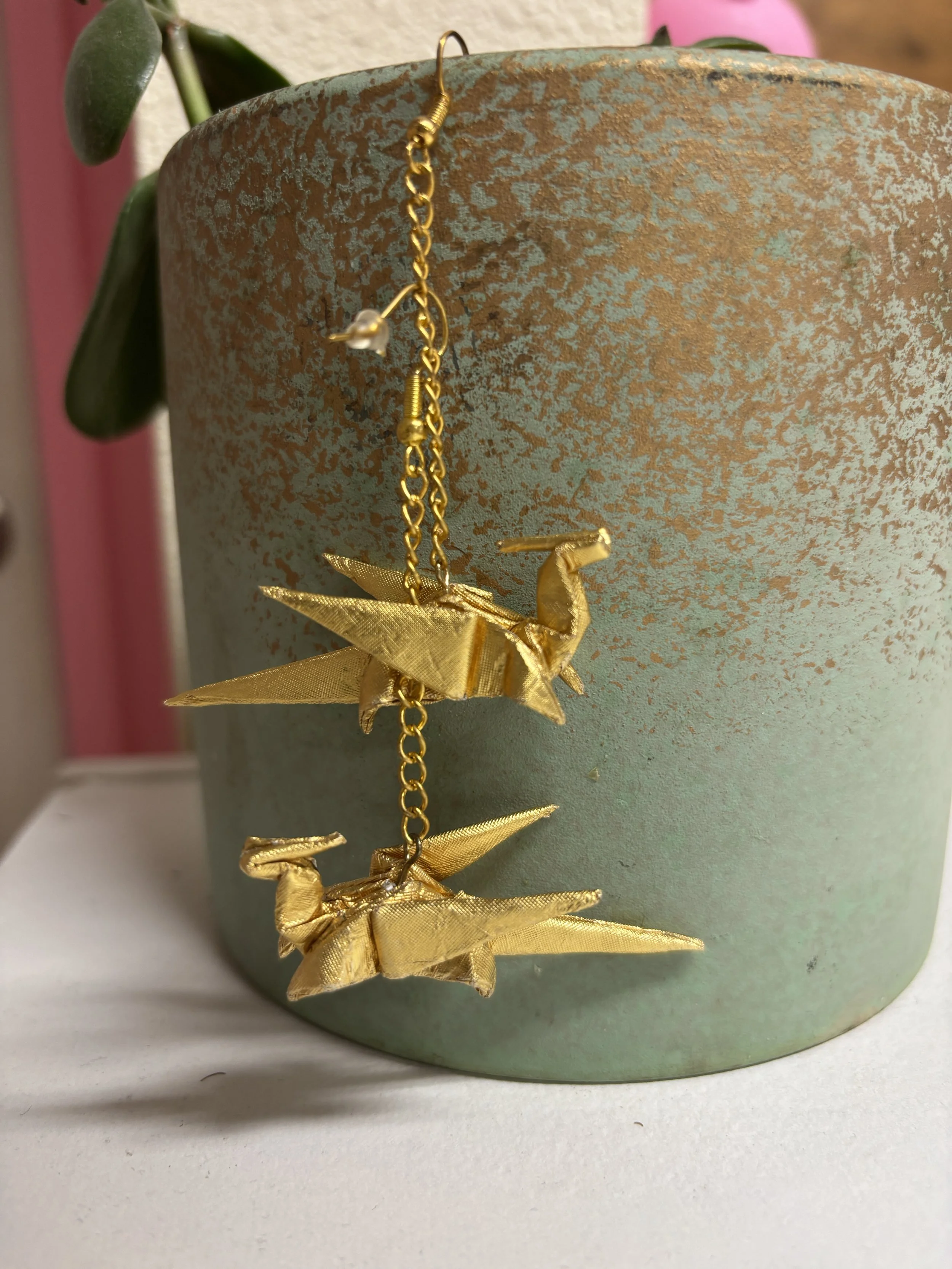 Pair of golden foil origami dragon earrings hanging from green floral pot