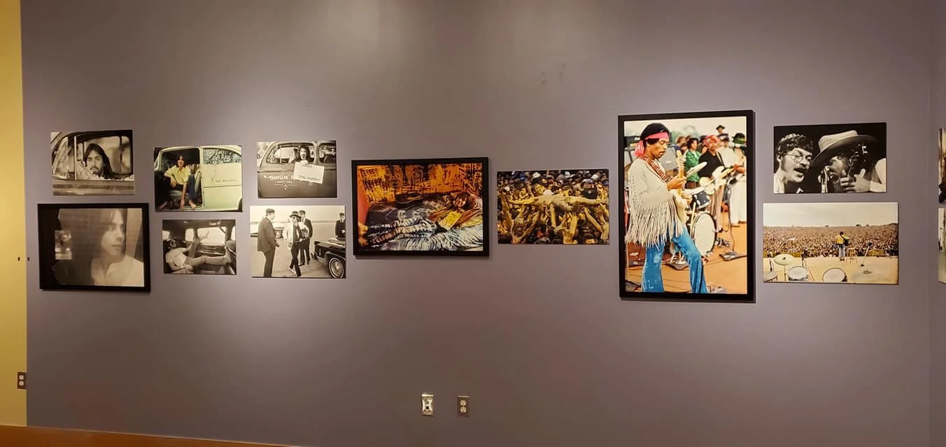 A gallery wall displaying various framed photographs, including black and white images and colorful scenes featuring people, animals, and landscapes.