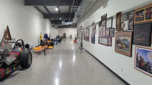 Museum hallway with framed pictures on the wall and various vehicles and exhibits on the floor.
