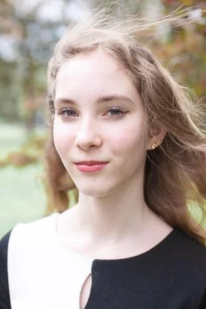 Portrait of a young woman outdoors with wind-blown hair and a slight smile.
