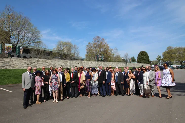 Group of people dressed formally and semi-formally standing outdoors in a parking lot on a sunny day.