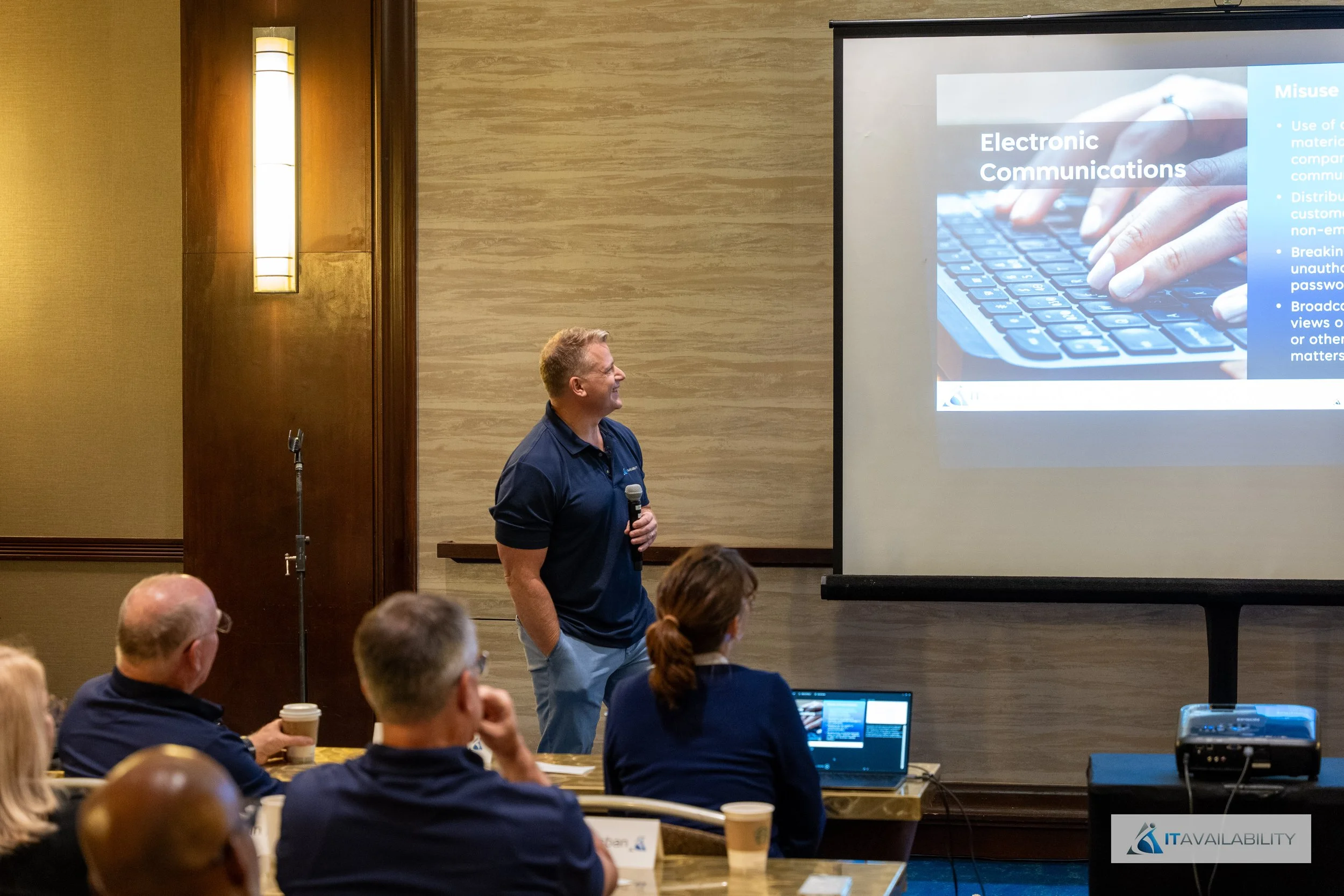 A man giving a presentation on electronic communications to a seated audience in a conference room.