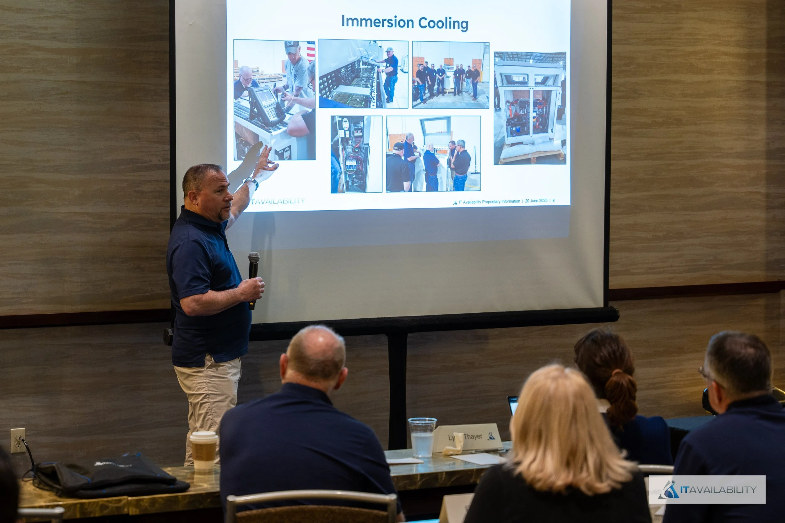 A man giving a presentation in a conference room, pointing to a slide titled 'Immersion Cooling' showing images of IT equipment and technicians.