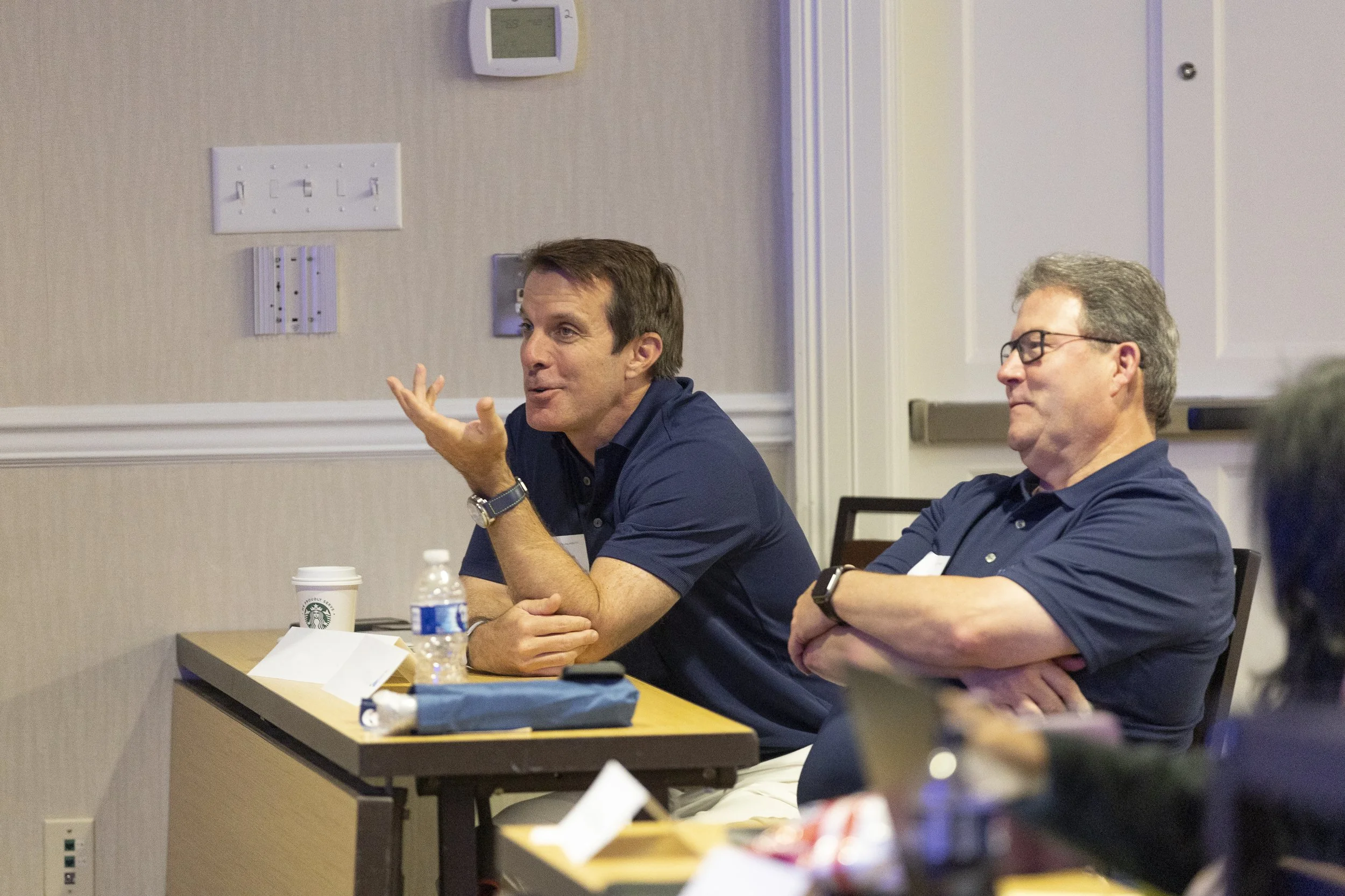 Two men seated at a table, engaged in a discussion during a meeting or conference.