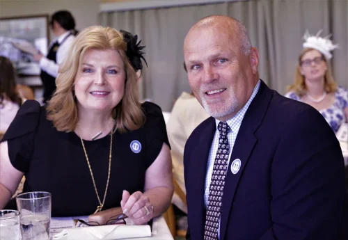 A smiling woman with blonde hair and a black dress sitting next to a smiling bald man in a suit at a formal event.