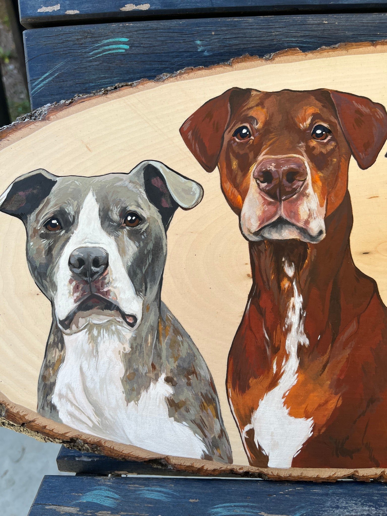 Painting of two dogs, a gray and white one on the left with a serious expression and a brown one on the right with a gentle look, on a wooden round plaque.