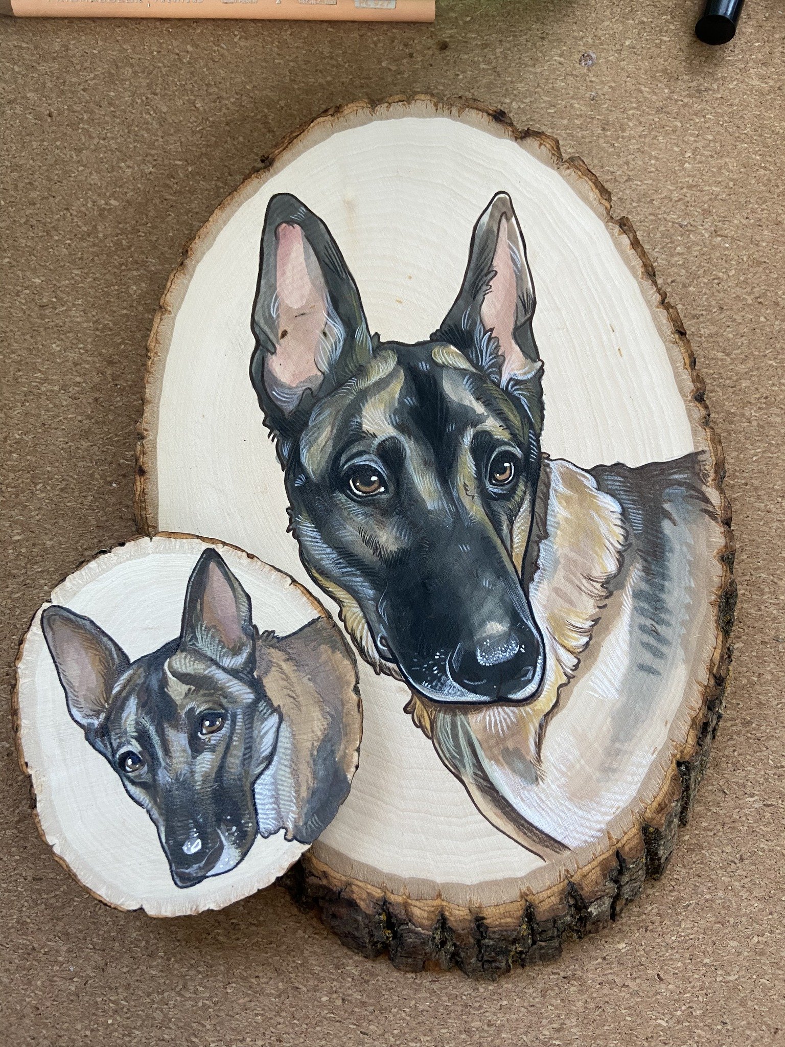 Painted wood slices depicting a Dutch Shepherd's head, with one larger and one smaller slice showing detailed portraits.