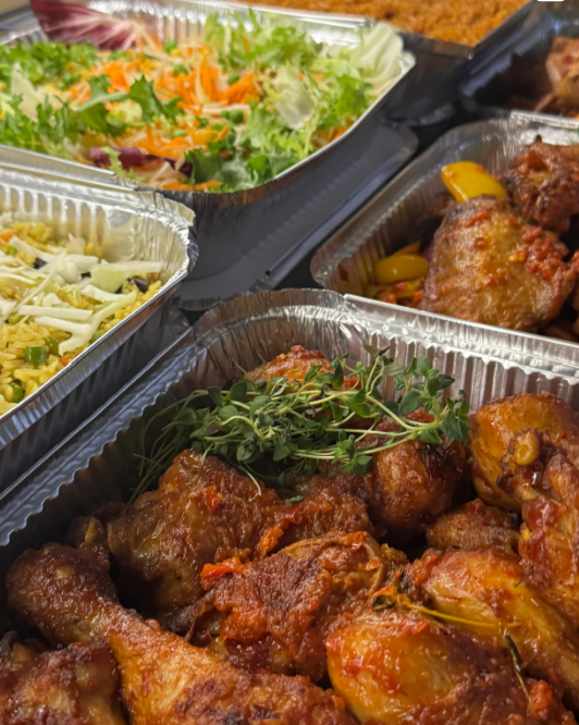 Aluminum trays with assorted food items including chicken drumsticks, rice, shredded cheese, green salad, and vegetable mix.