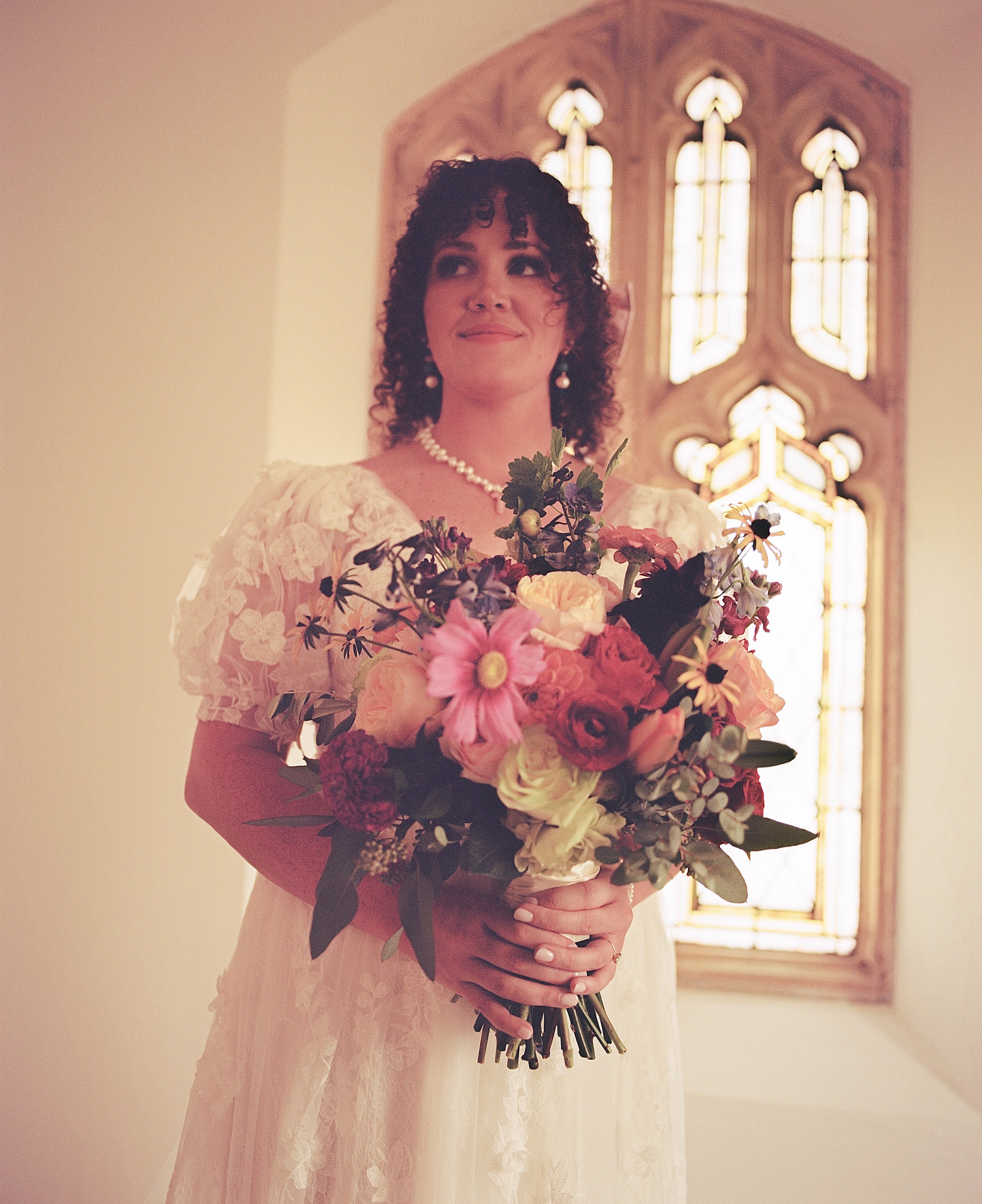 A woman in a wedding dress holding a bouquet of flowers, standing in front of stained glass window.