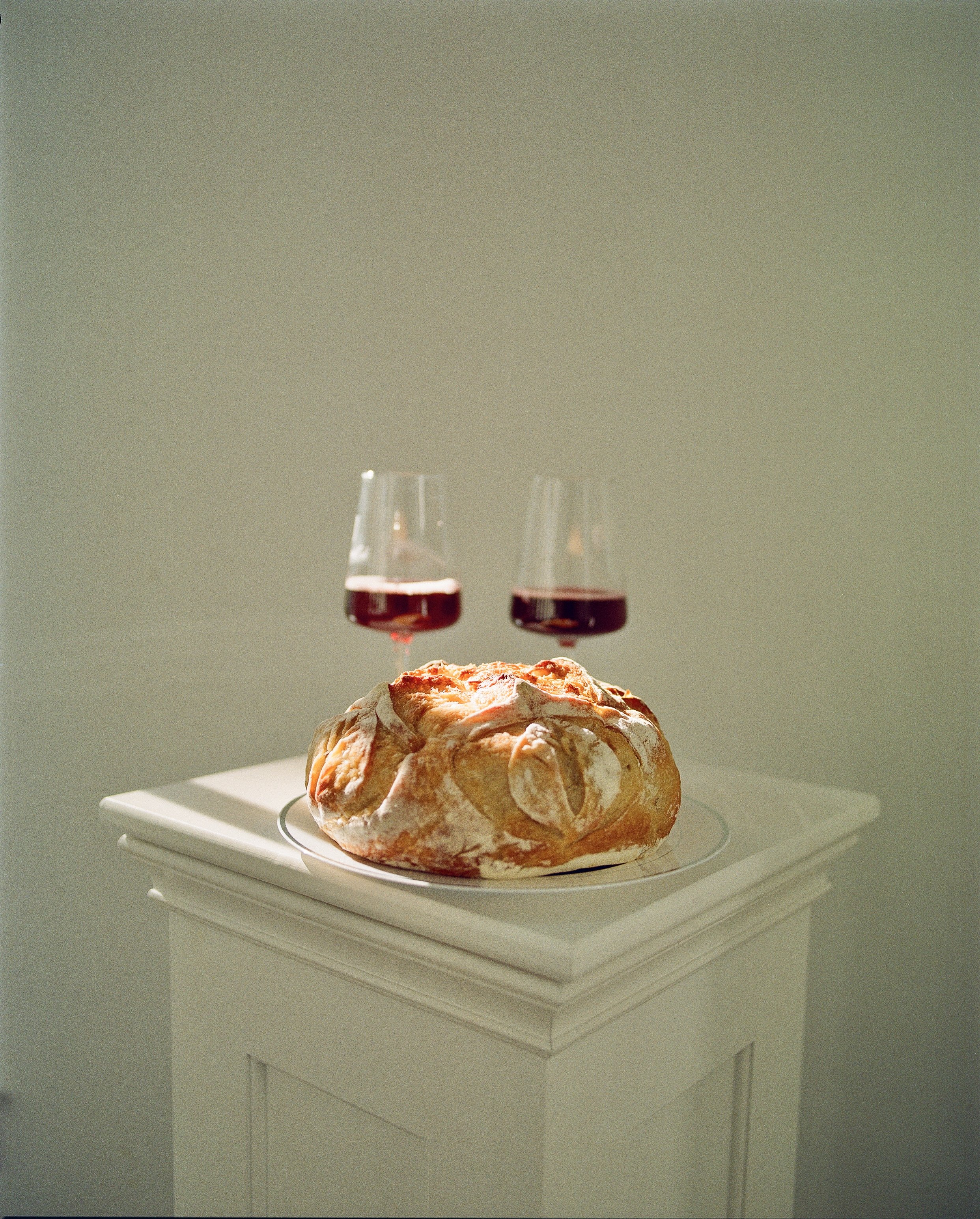 A loaf of bread with two glasses of red wine on a white pedestal table.