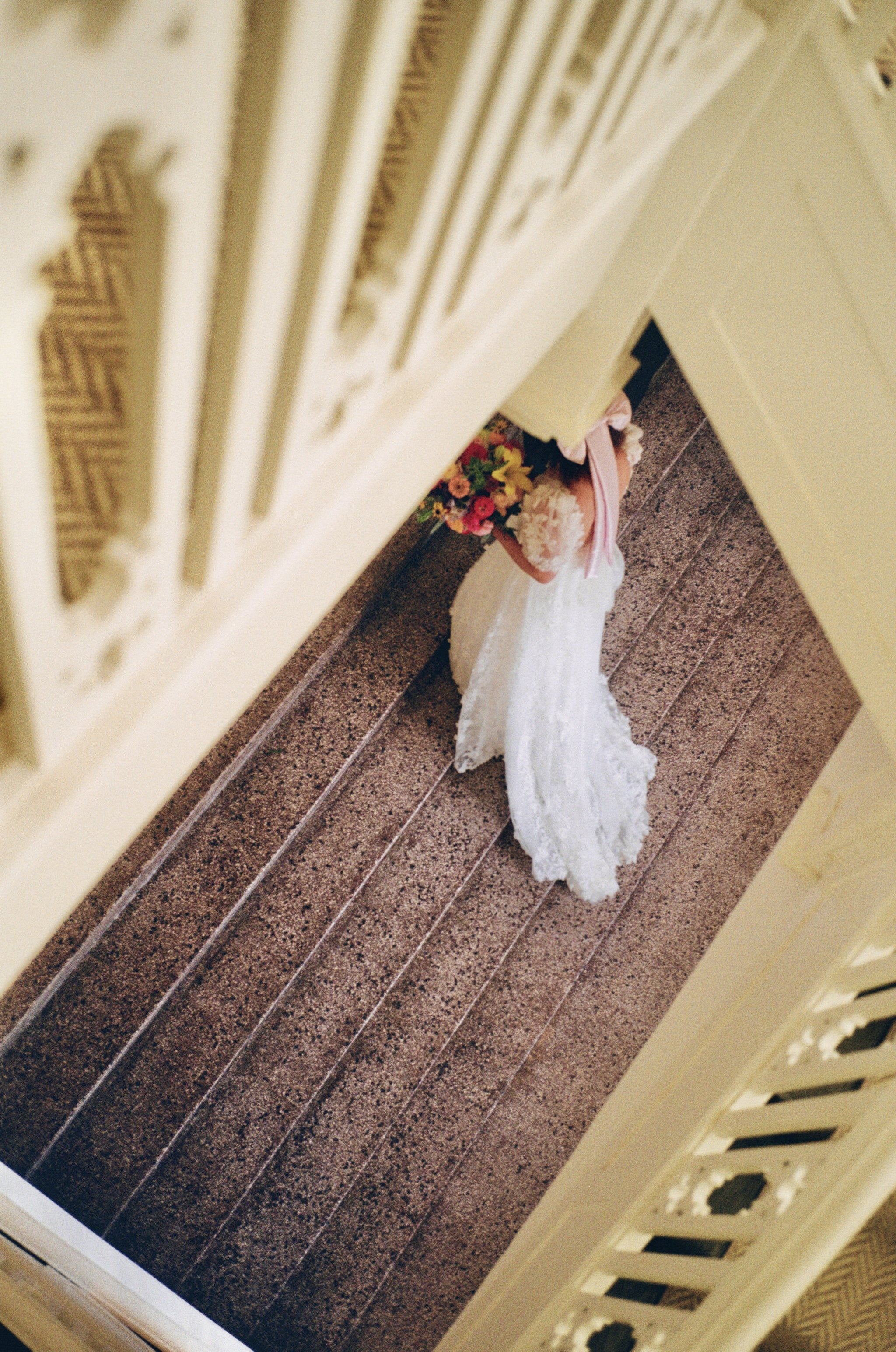A wedding dress and bouquet are seen from above, positioned against a staircase wall with decorative screen details.