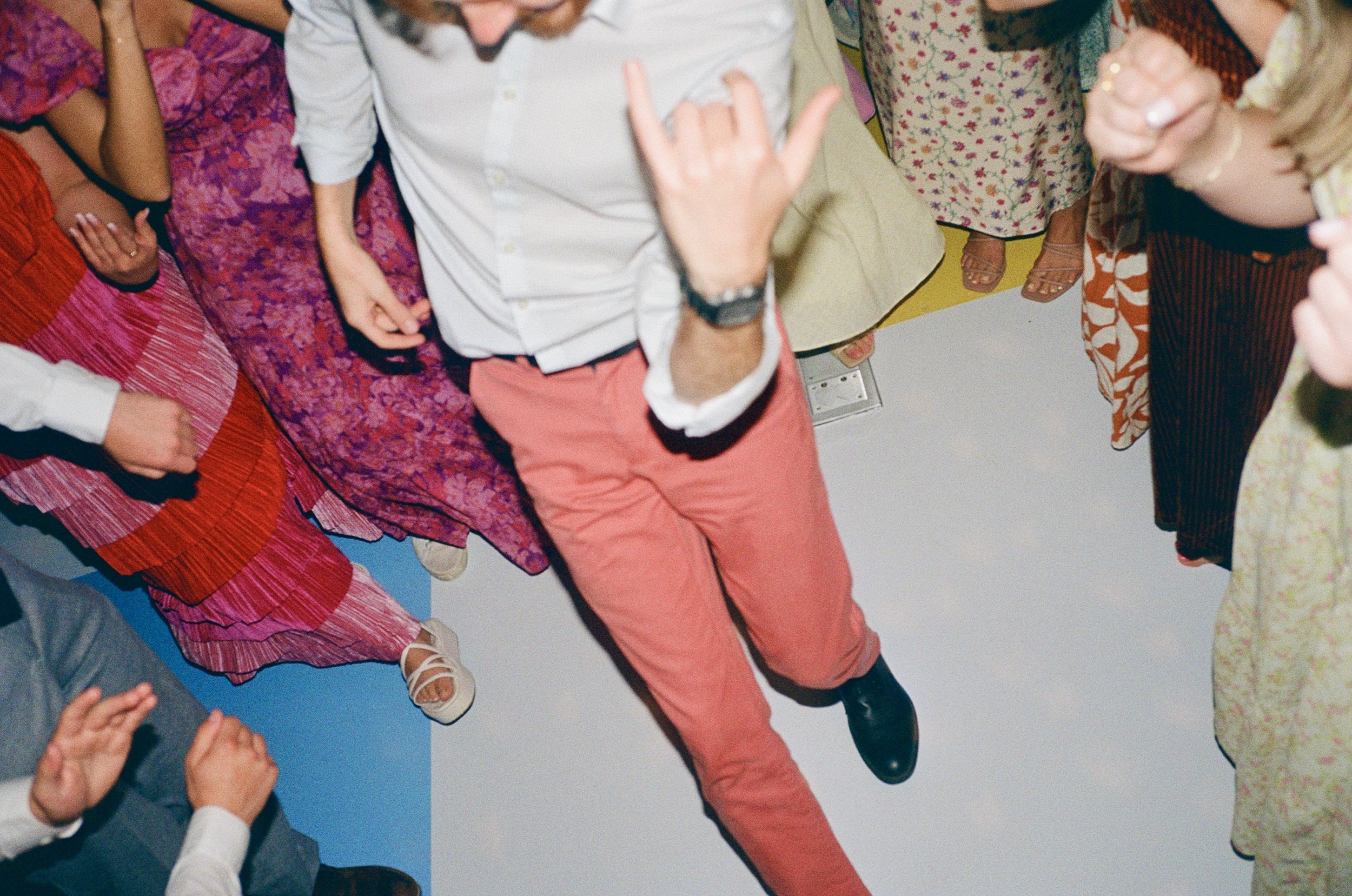 People gathered in a circle, with one person making a rock and roll hand gesture and others clapping or holding hands, at a social event or celebration.