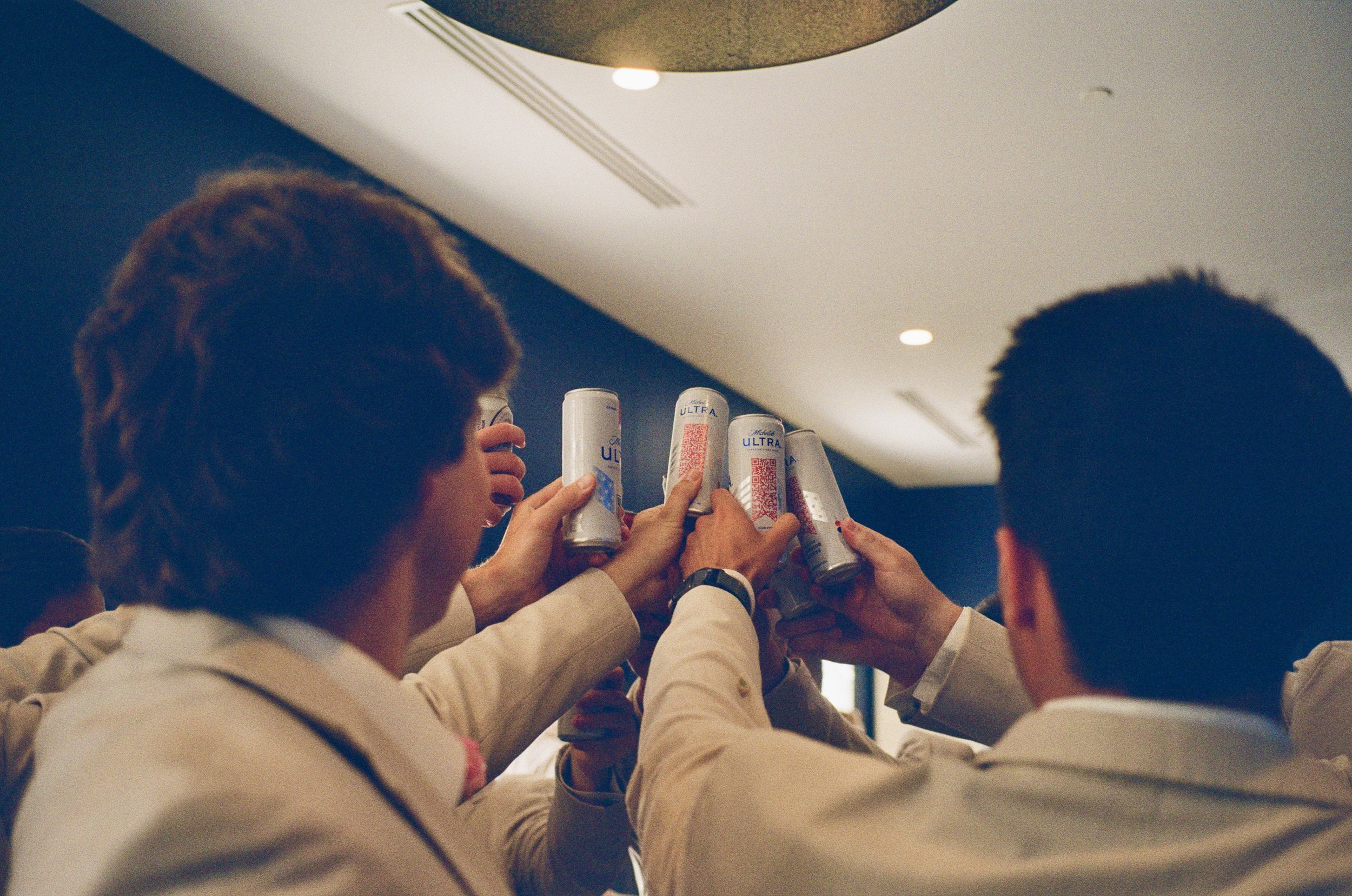 Group of people in formal attire raising cans of Red Bull energy drink in a toast.