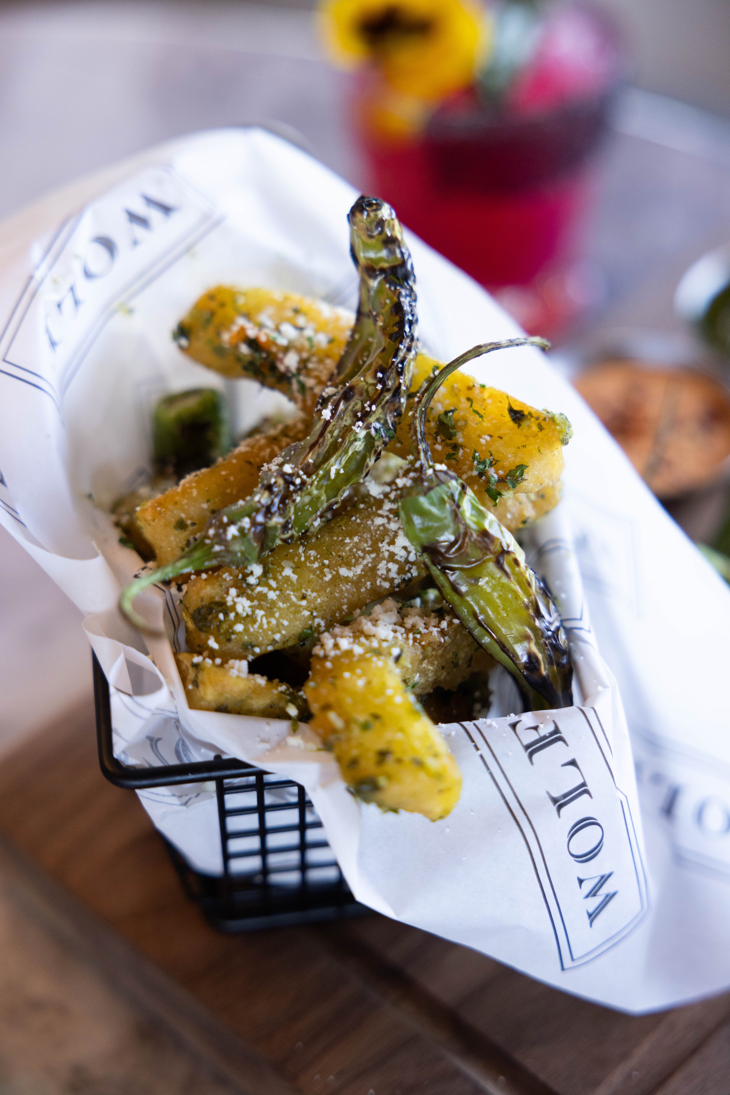 Basket of fried yellow squash and fried green chili peppers sprinkled with cheese, lined with newspaper paper.