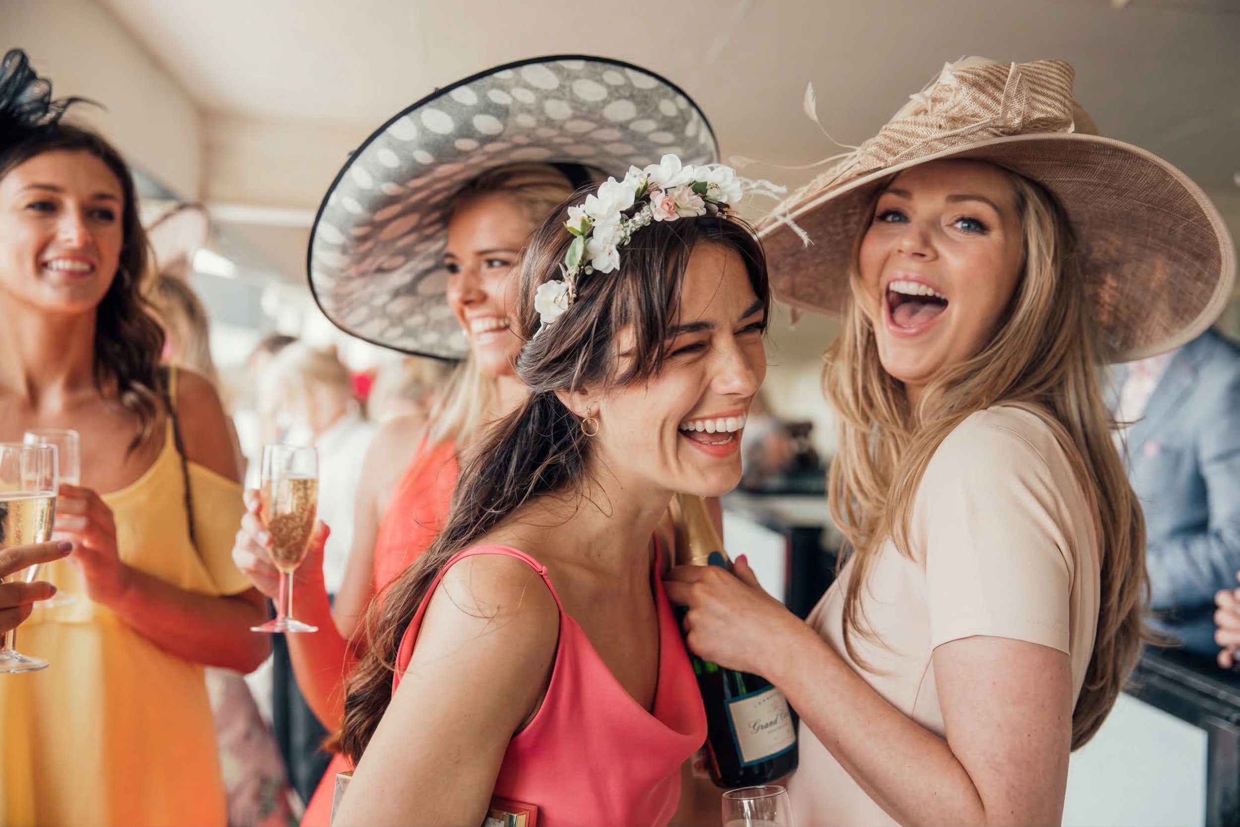 Women celebrating at a party, wearing fancy dresses and hats, holding glasses of champagne.