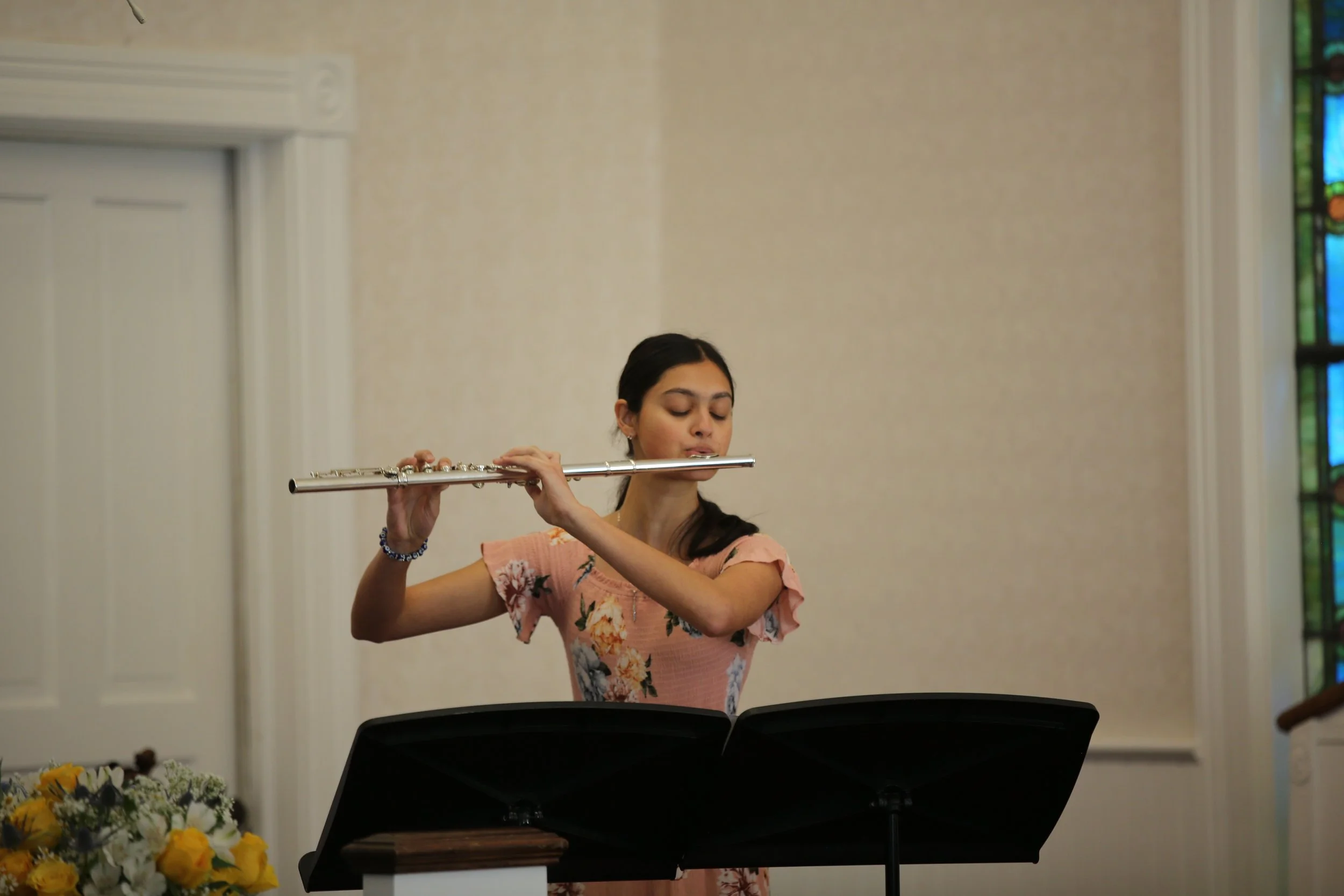 Young woman with dark hair playing a silver flute during a music performance in a church or concert hall.