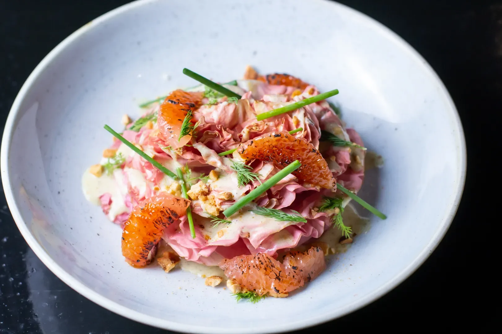 Salad with pink ham, orange clementine slices, green herbs, chopped nuts, and creamy dressing, served on a white plate.