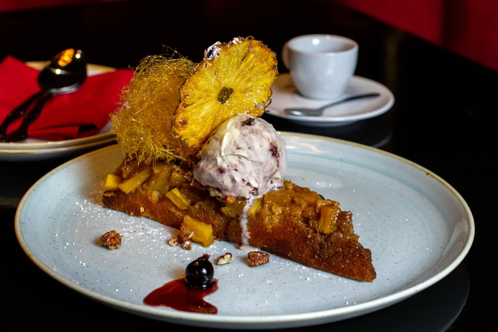 Slice of fruit crumble pie topped with ice cream, garnished with caramelized pineapple, a honeycomb, and a dollop of berry sauce on the side.
