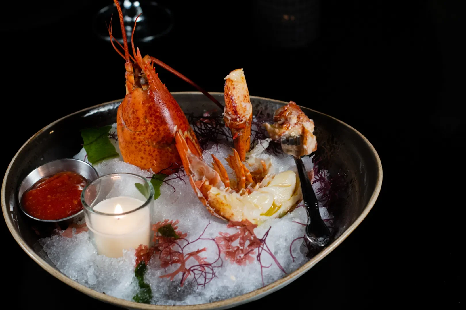 Lobster tail on ice with dipping sauces, lemon, and a candle.