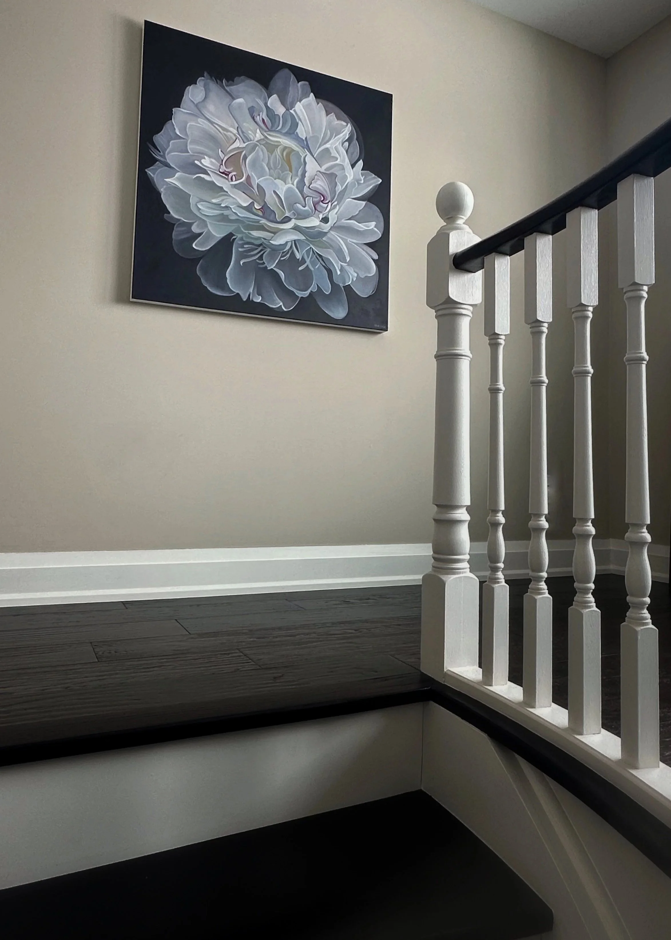 Interior view of a staircase landing with a painting of a white flower on the wall and a white wooden railing.