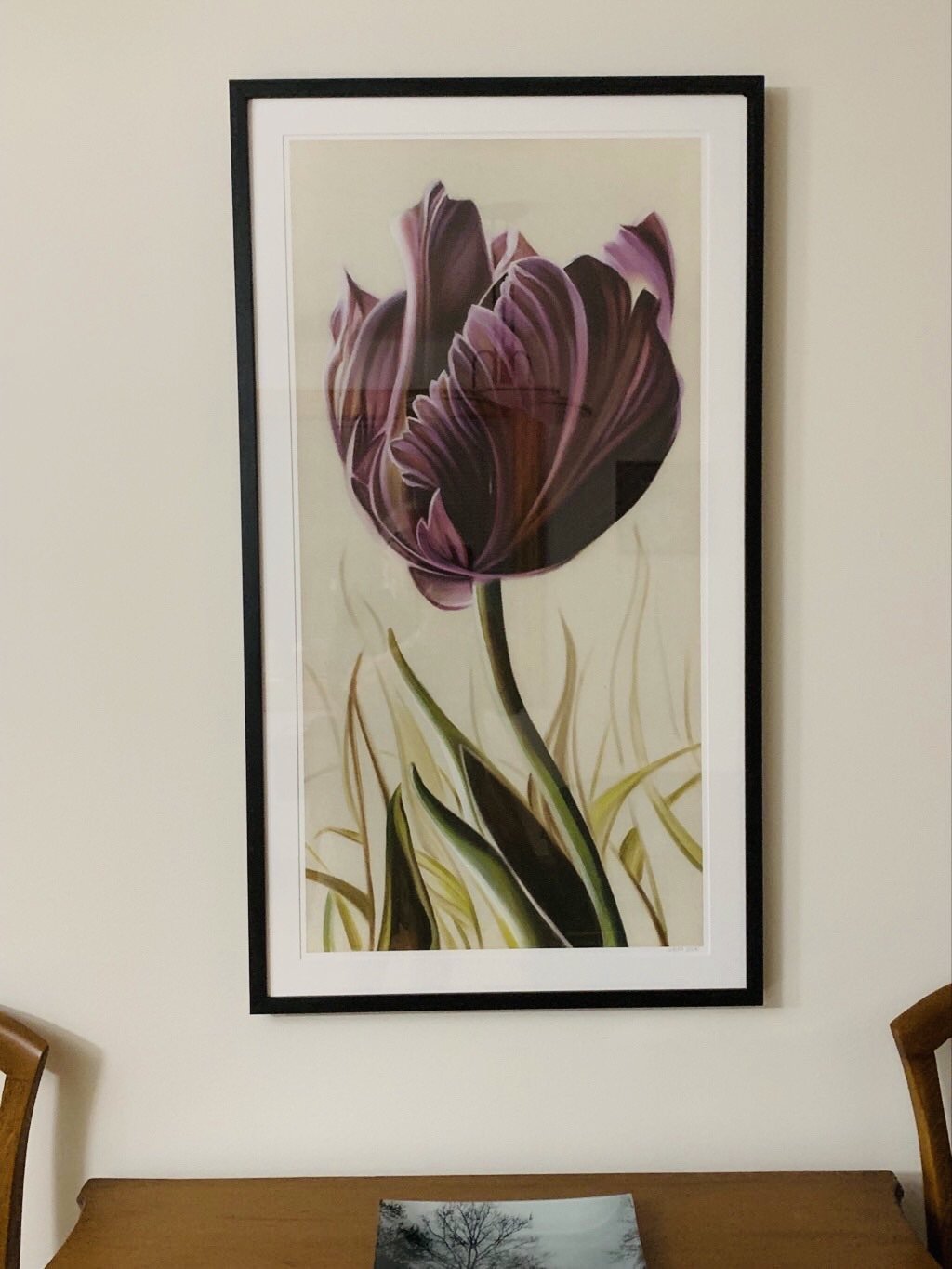 Framed painting of a purple and pink tulip with green and yellow blades of grass on a beige background in a dining room.