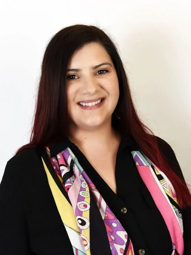 A woman with long dark hair and a friendly smile, wearing a black blouse and a colorful patterned scarf.