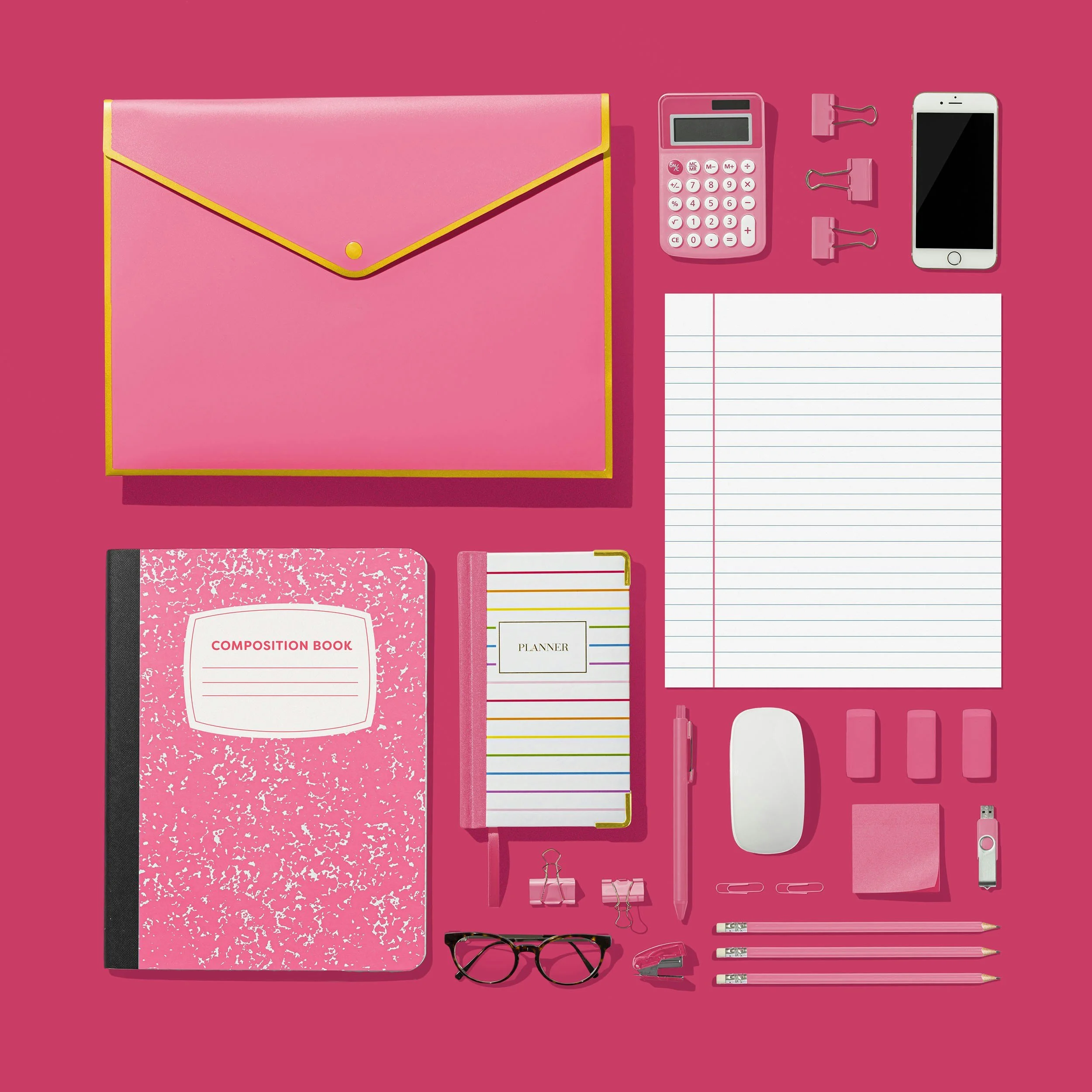 Collection of pink and white stationery and office supplies arranged on a pink background, including notebooks, pens, a calculator, binder clips, eyeglasses, and a stapler.