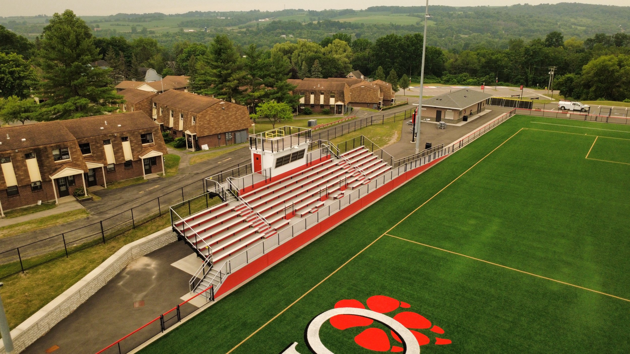 Aerial view of a football stadium with a large paw logo painted on the field, surrounded by a corner of residential buildings and trees in the background.