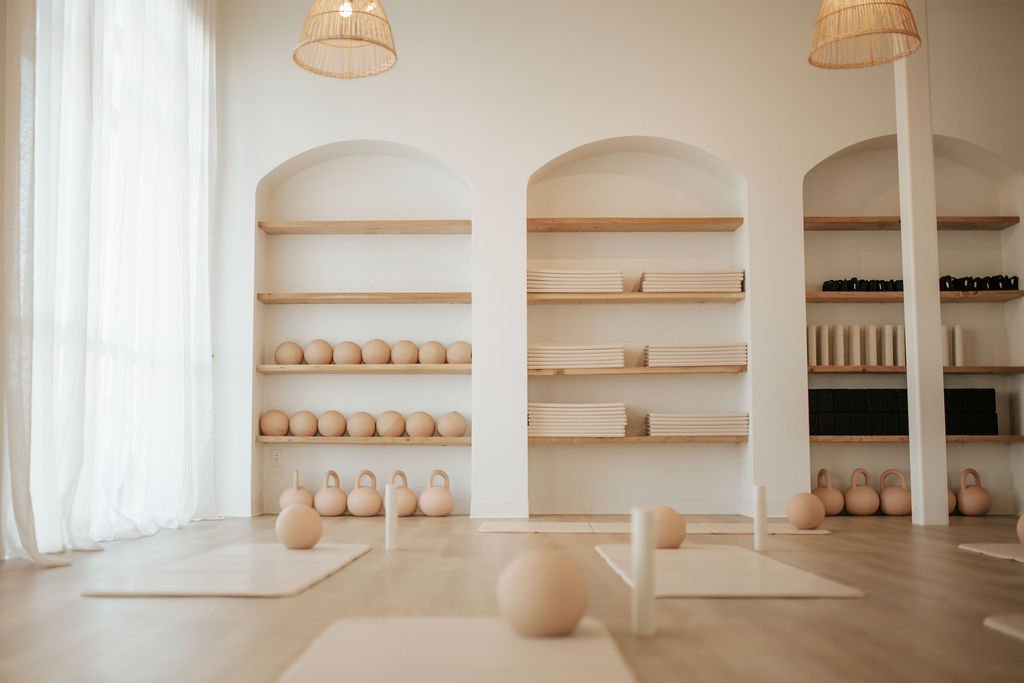 Yoga studio with mats, bolsters, and wall mirrors in a bright room with hanging pendant lights.