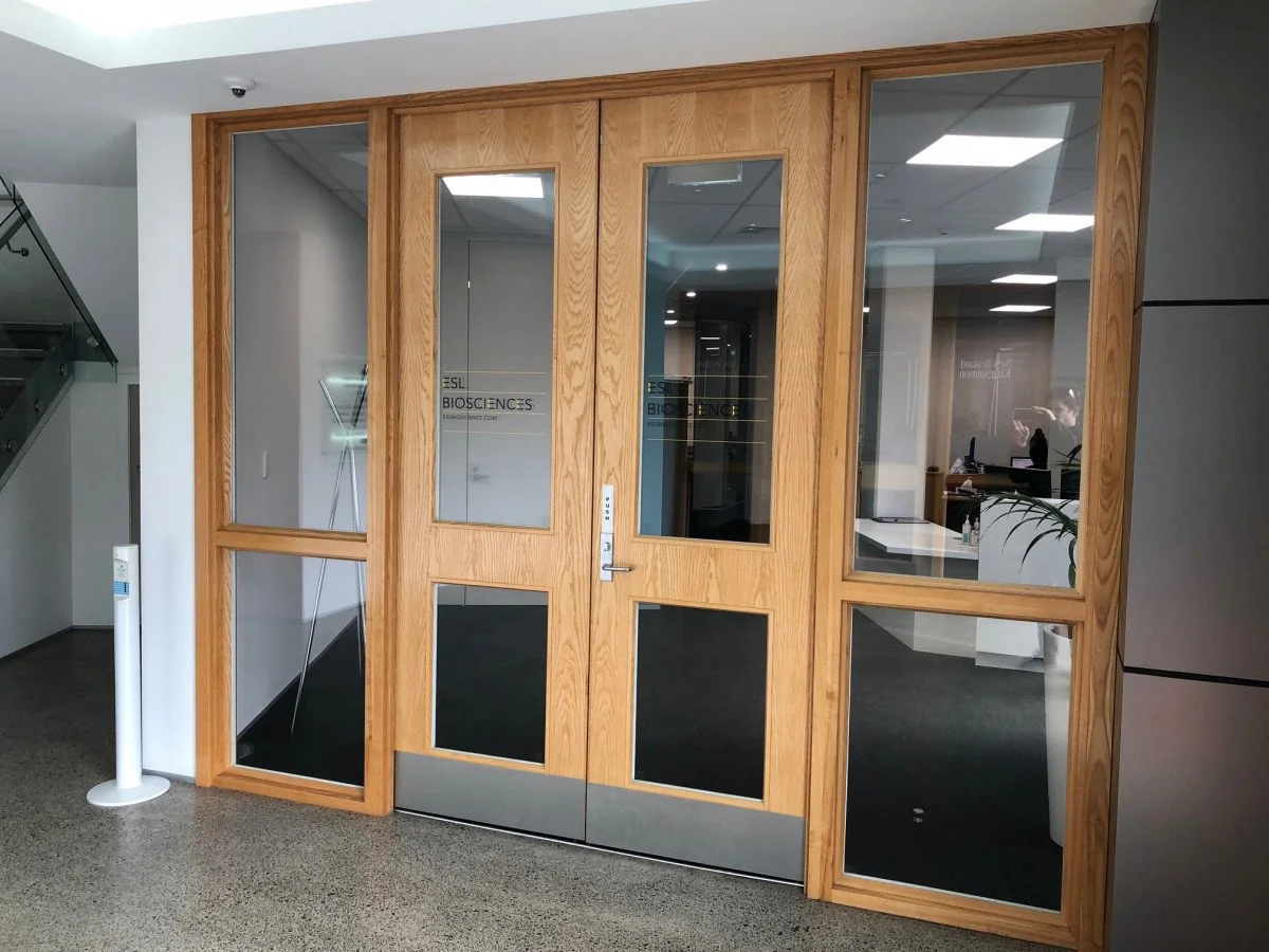 Wooden-framed glass doors leading to an office space, with a sign reading 'ESL BIOSCIENCES' on the door.