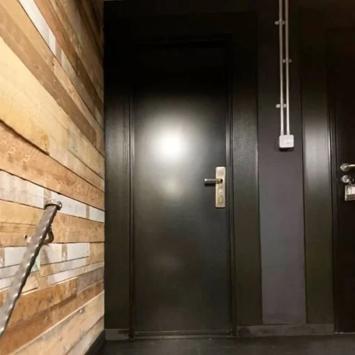 A black door in a room with dark walls and a wood-paneled wall to the left.