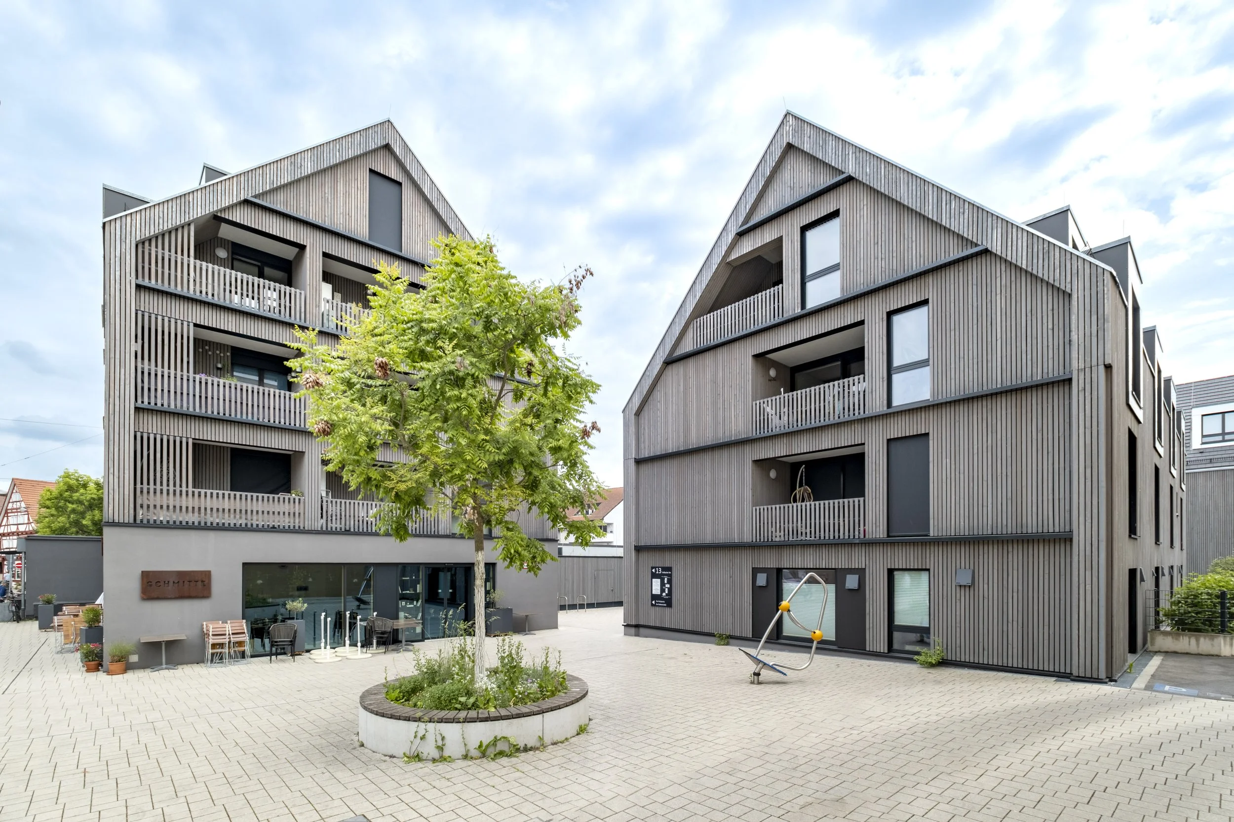 Moderne, dreistöckige Holzhäuser mit Balkonen und einer kleinen Parkanlage mit Baum in der Mitte