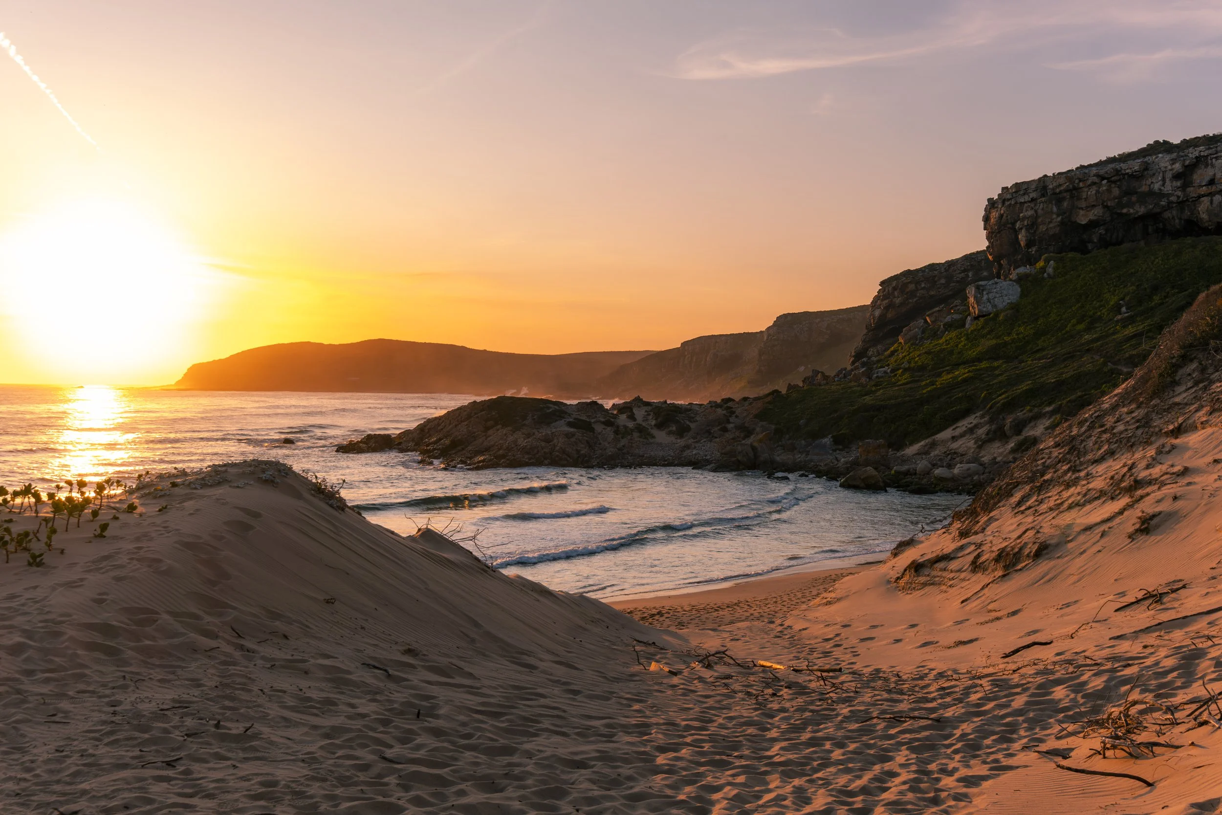 Sonnenuntergang am Strand mit Sanddünen, Felsen und dem Meer