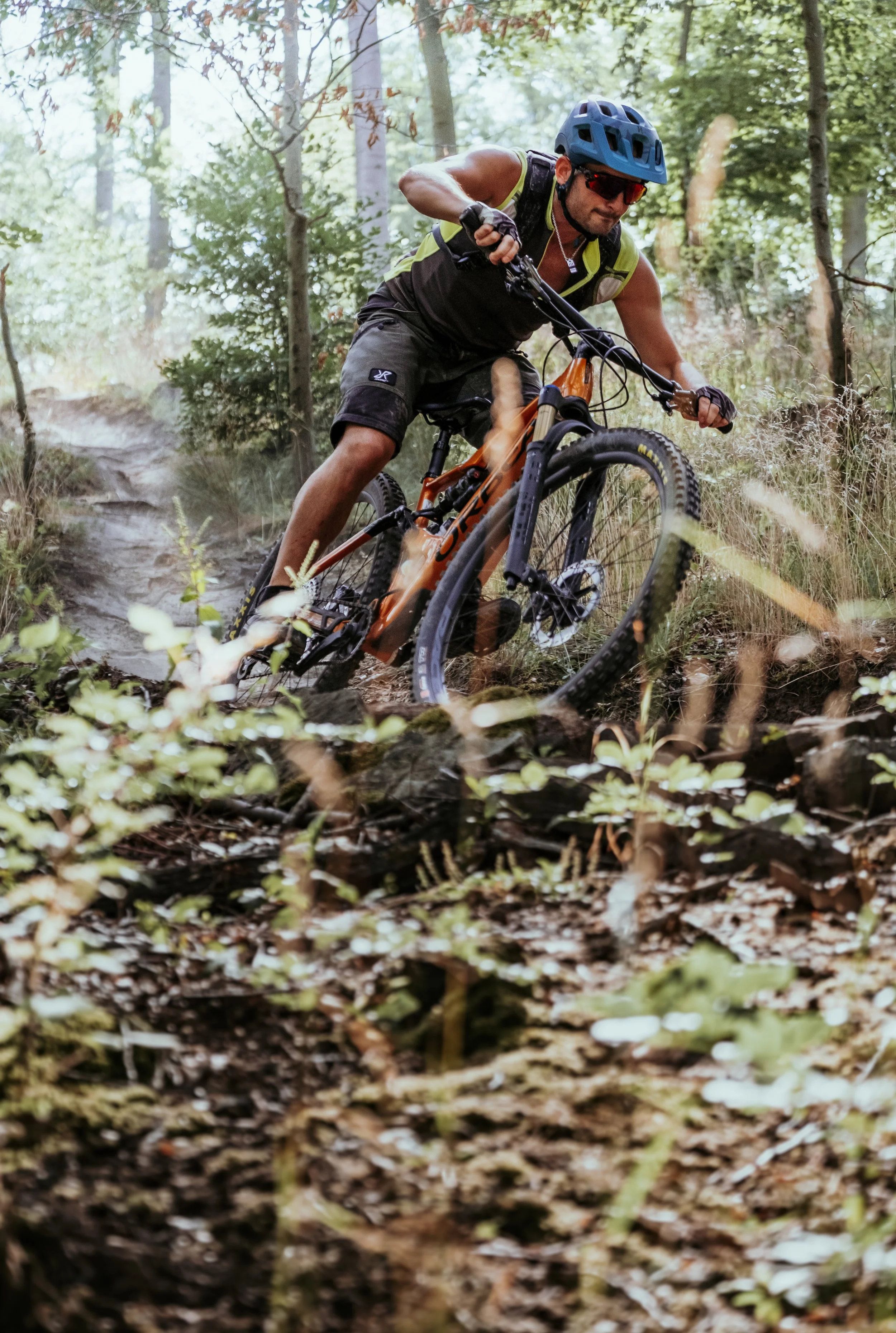 Mann beim Mountainbiken auf einem bewaldeten Trampelpfad, trägt Helm und Sonnenbrille.