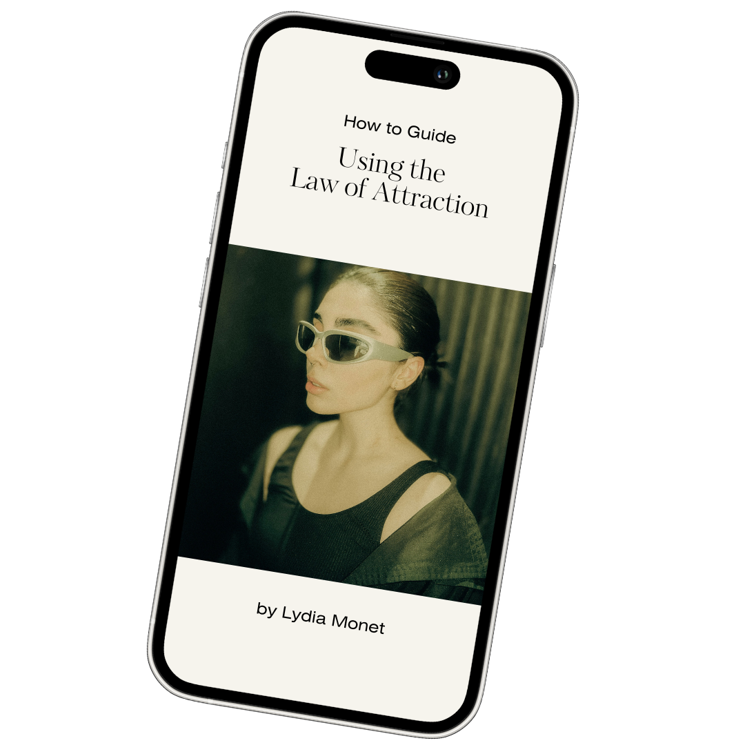 Smartphone displaying a guide titled 'How to Guide Using the Law of Attraction' with a photo of a woman wearing sunglasses on the cover and the author's name, Lydia Monet.