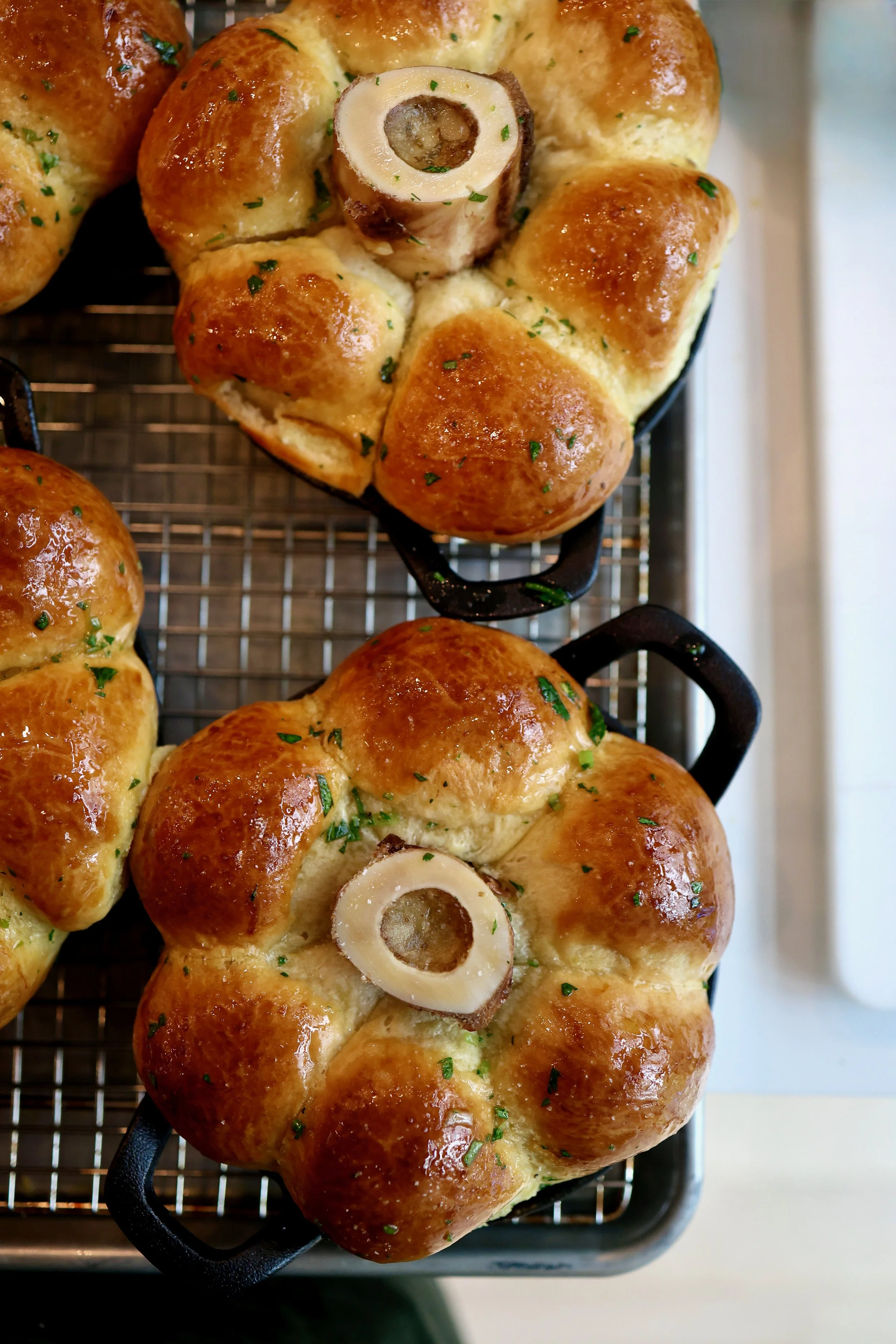 Golden-brown baked rolls garnished with chopped parsley and featuring slices of cooked marrow or bone marrow in the center, placed on a black metal rack.