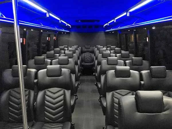 Interior of a luxury bus or limousine with black leather seats and blue LED lighting.